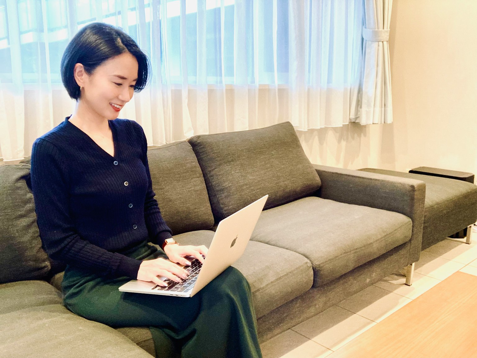 젊은 여성이 밝은 실내에서 소파에 앉아 노트북으로 작업하고 있는 모습