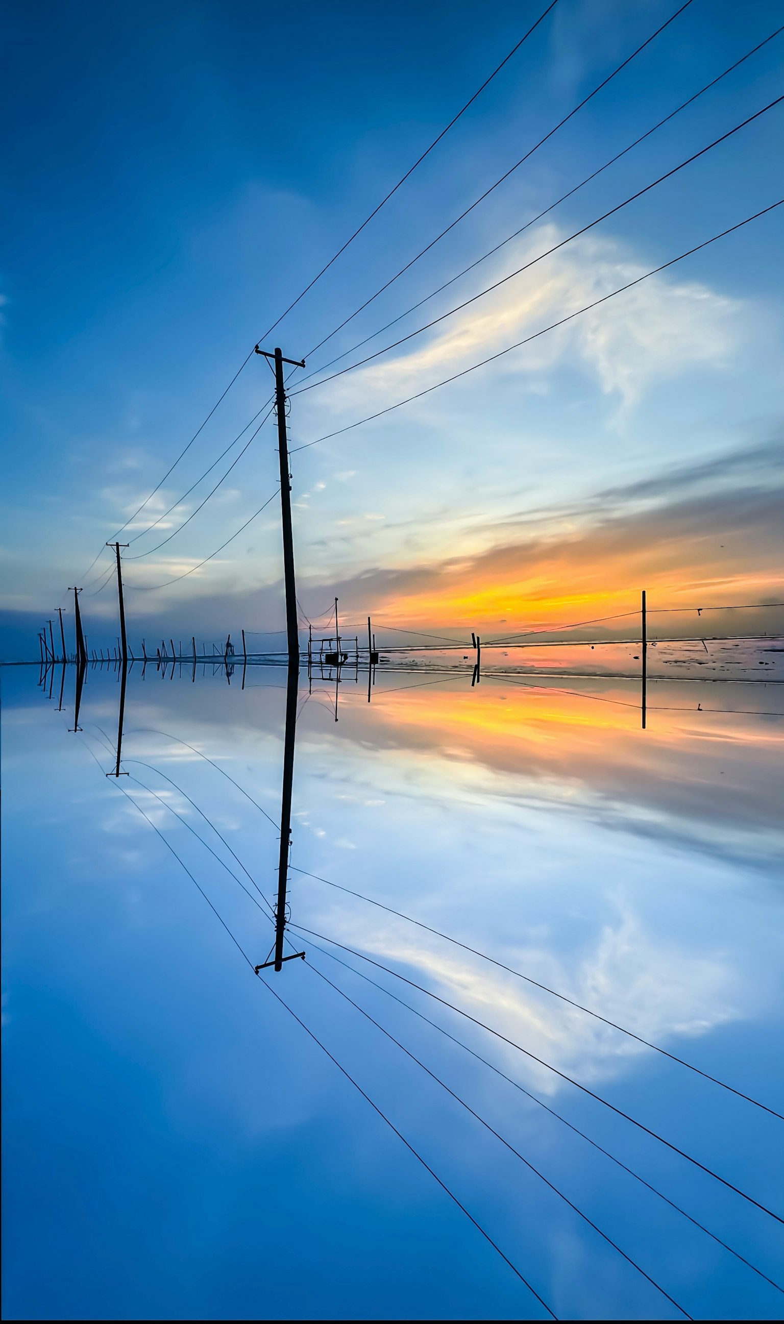 Strommasten, die sich im ruhigen Wasser bei Sonnenuntergang mit einem lebendigen blauen Himmel spiegeln