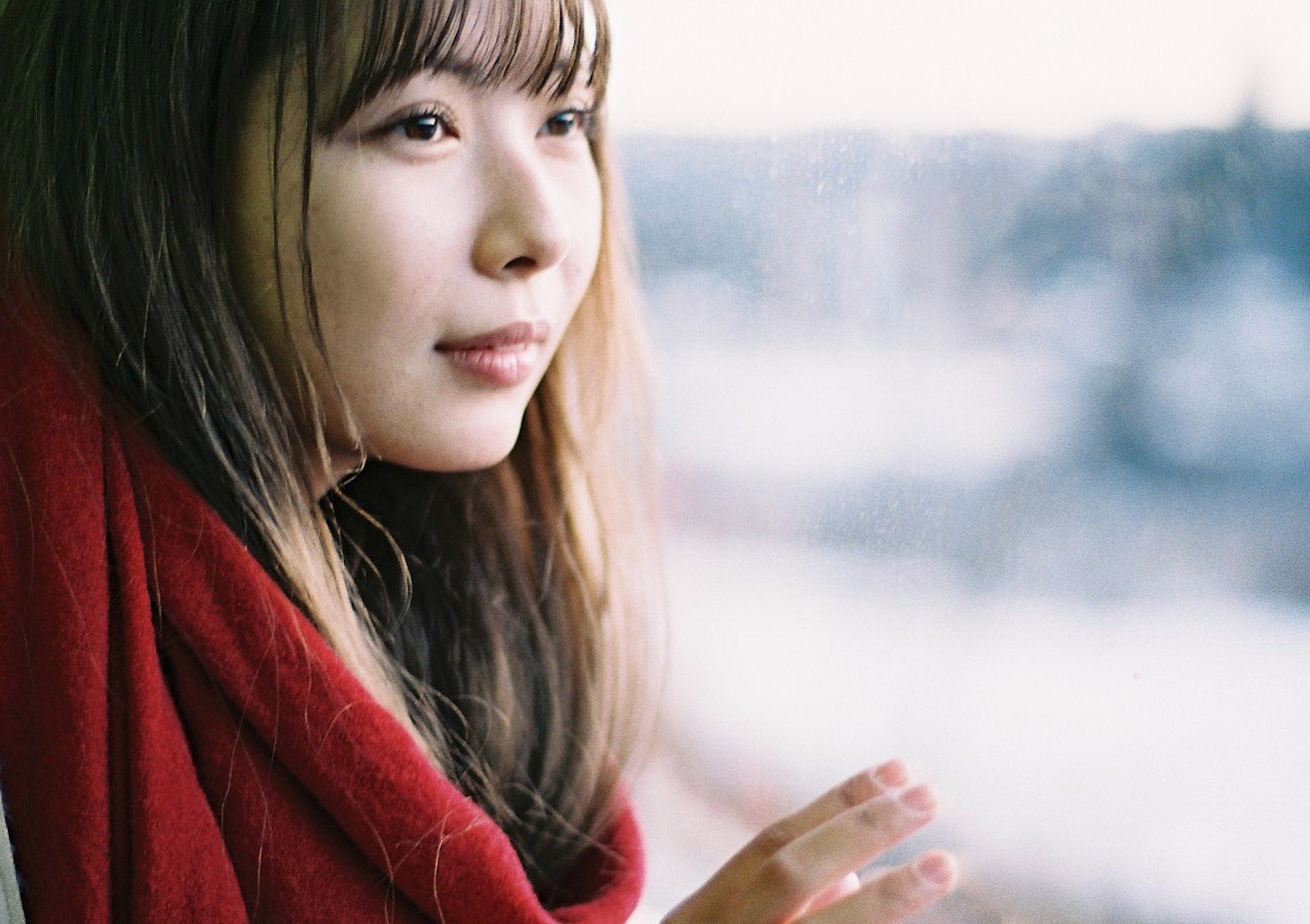 赤いコートの女性が手を添えて微笑むポートレート