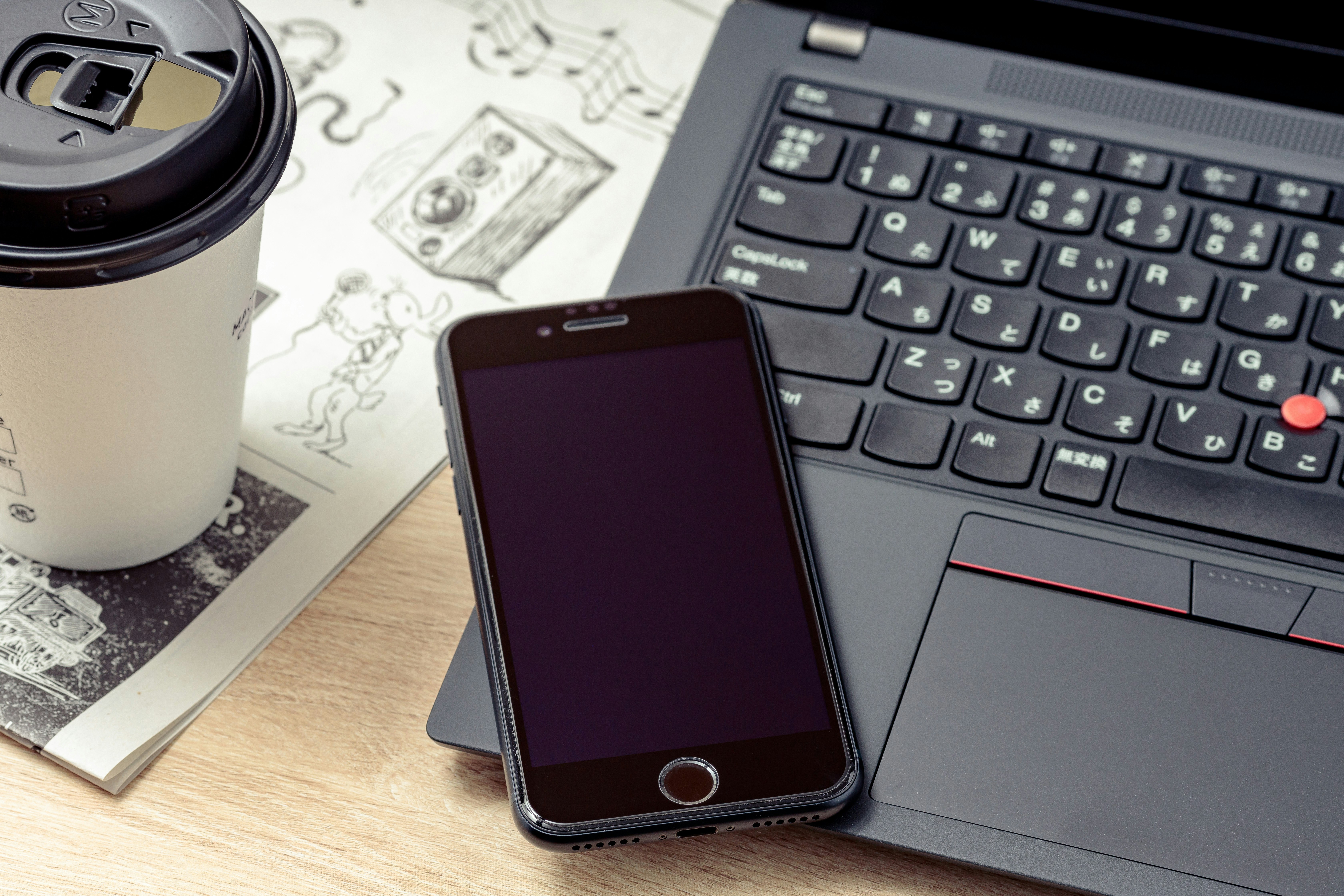 コーヒーと新聞、スマホとノートPCが並ぶビジネスデスクの風景