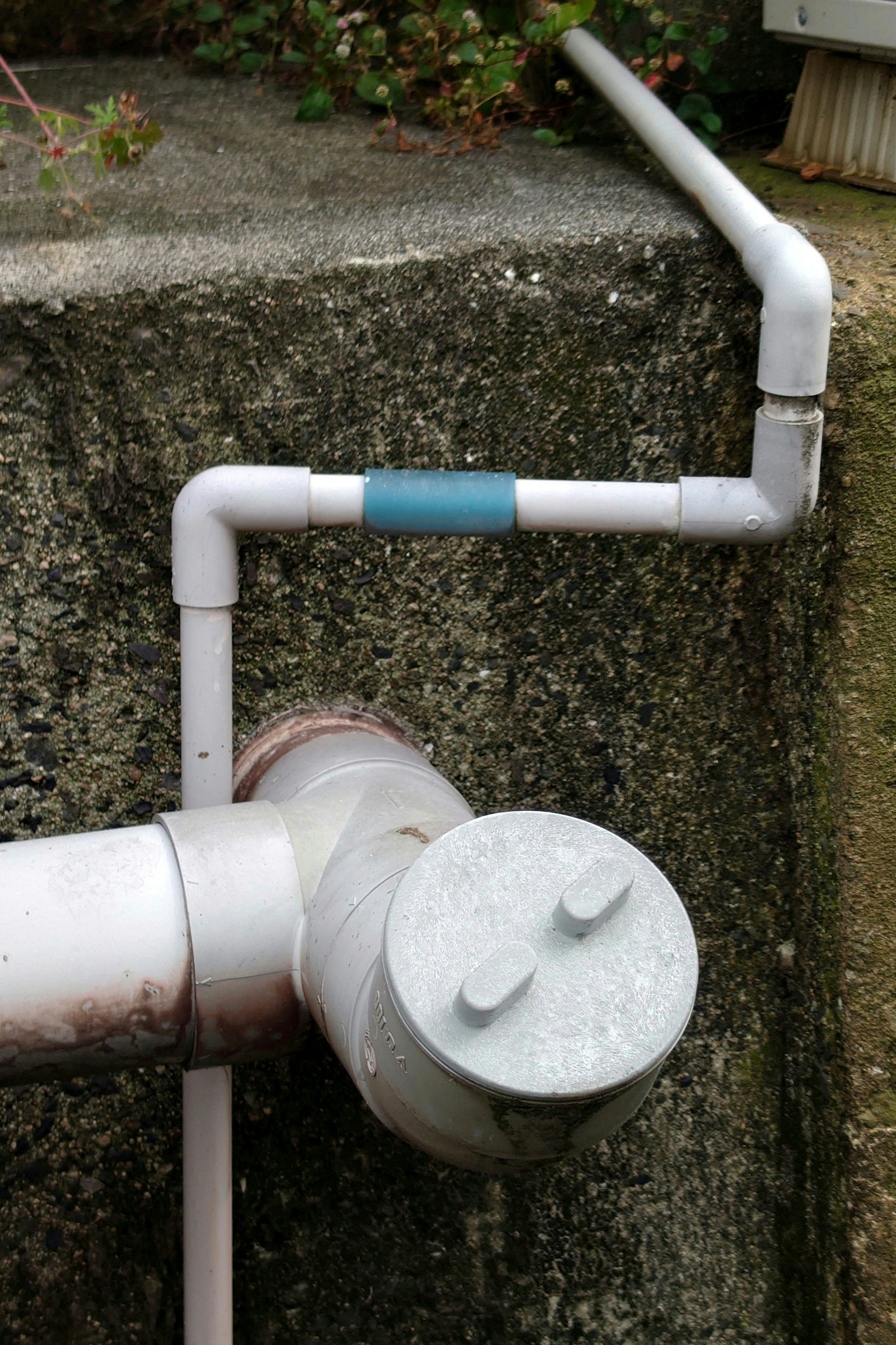 Tuberías blancas y una válvula circular cerca de una pared de concreto