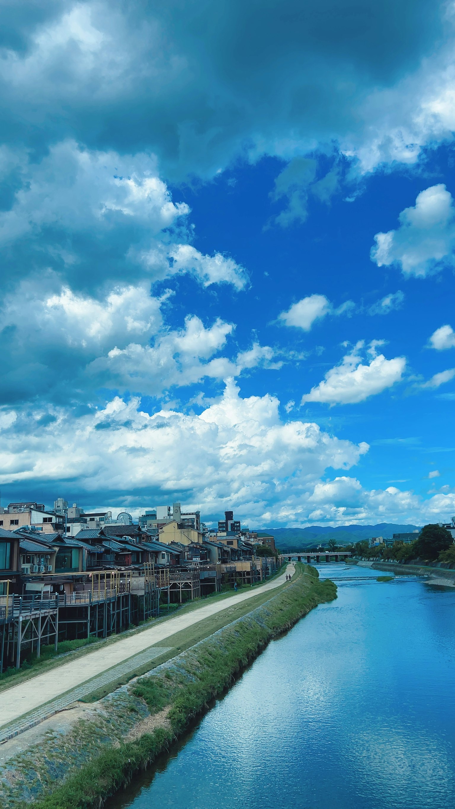 Scenic view of a river with buildings alongside under a blue sky and fluffy clouds