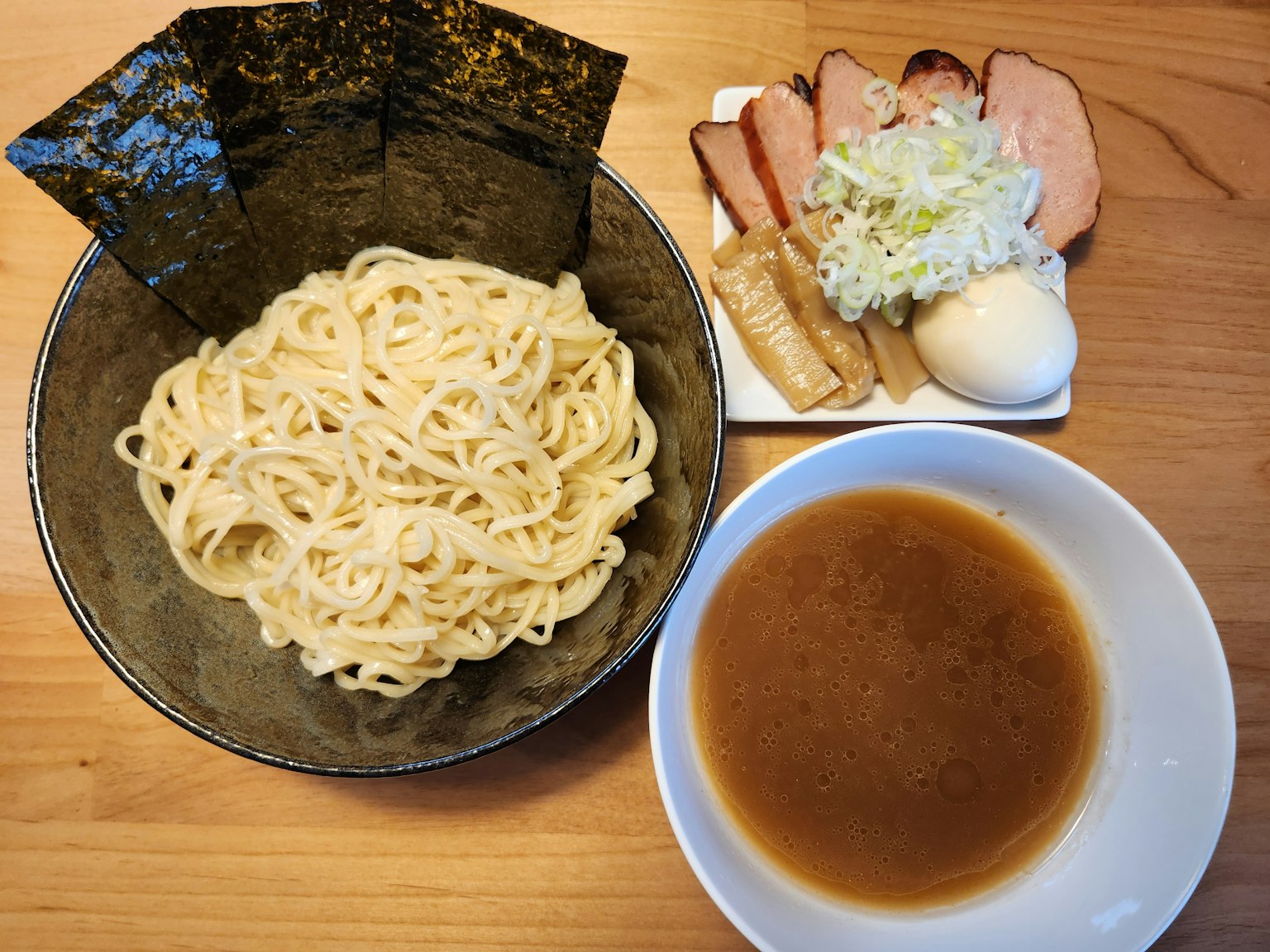 Mie tebal disajikan dalam mangkuk dengan saus celup dan pelengkap chashu serta kol