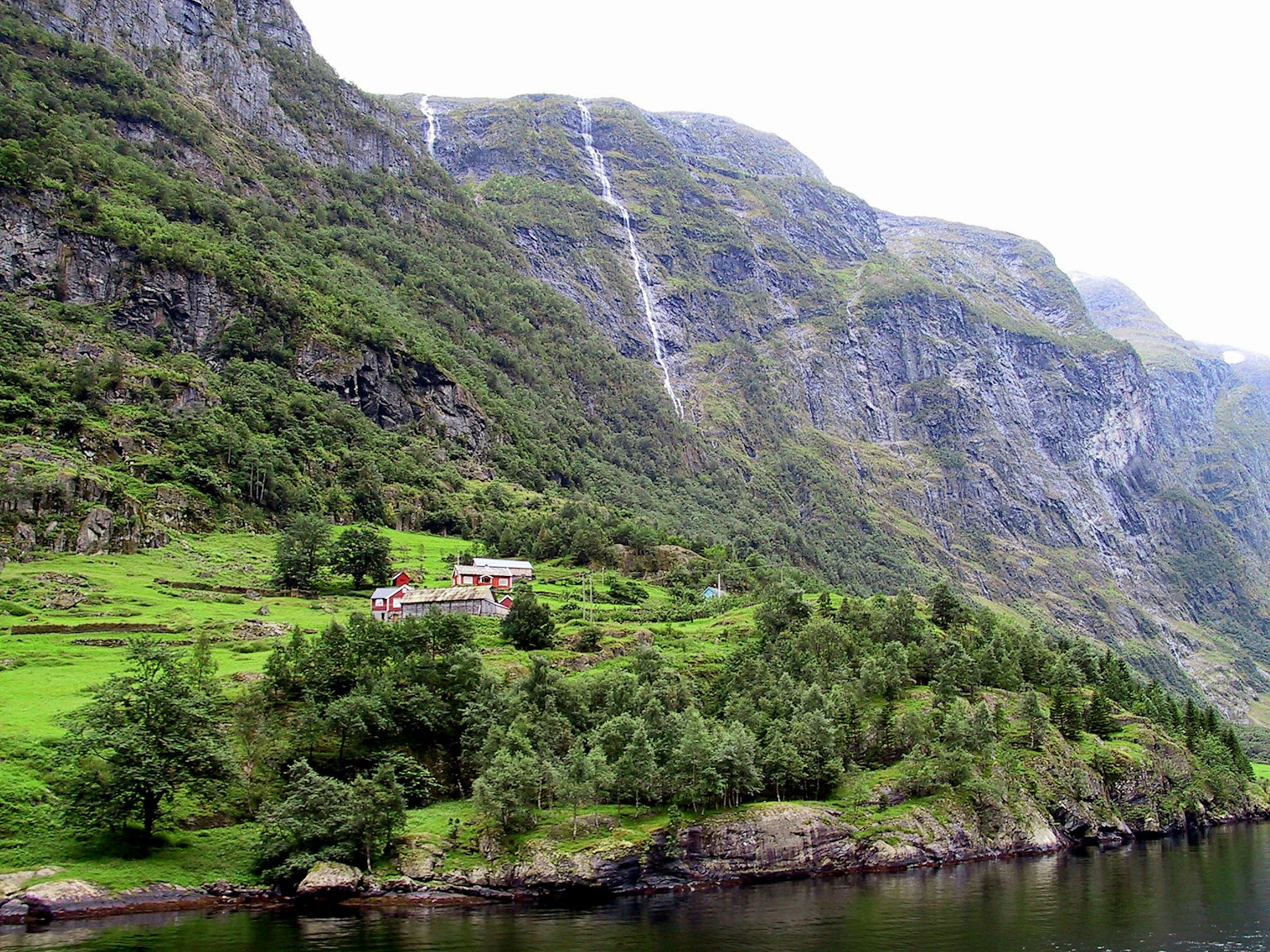 Vue pittoresque d'un fjord avec des collines verdoyantes et des cascades près d'un lac tranquille avec une maison