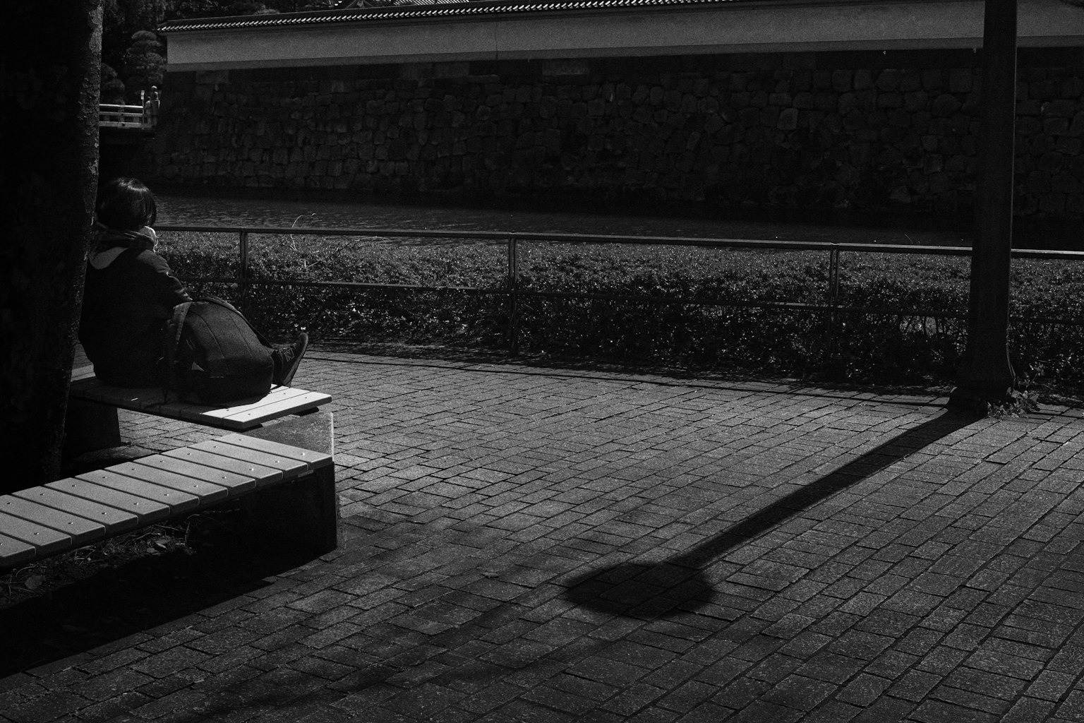 Photo en noir et blanc d'une personne assise sur un banc avec une longue ombre