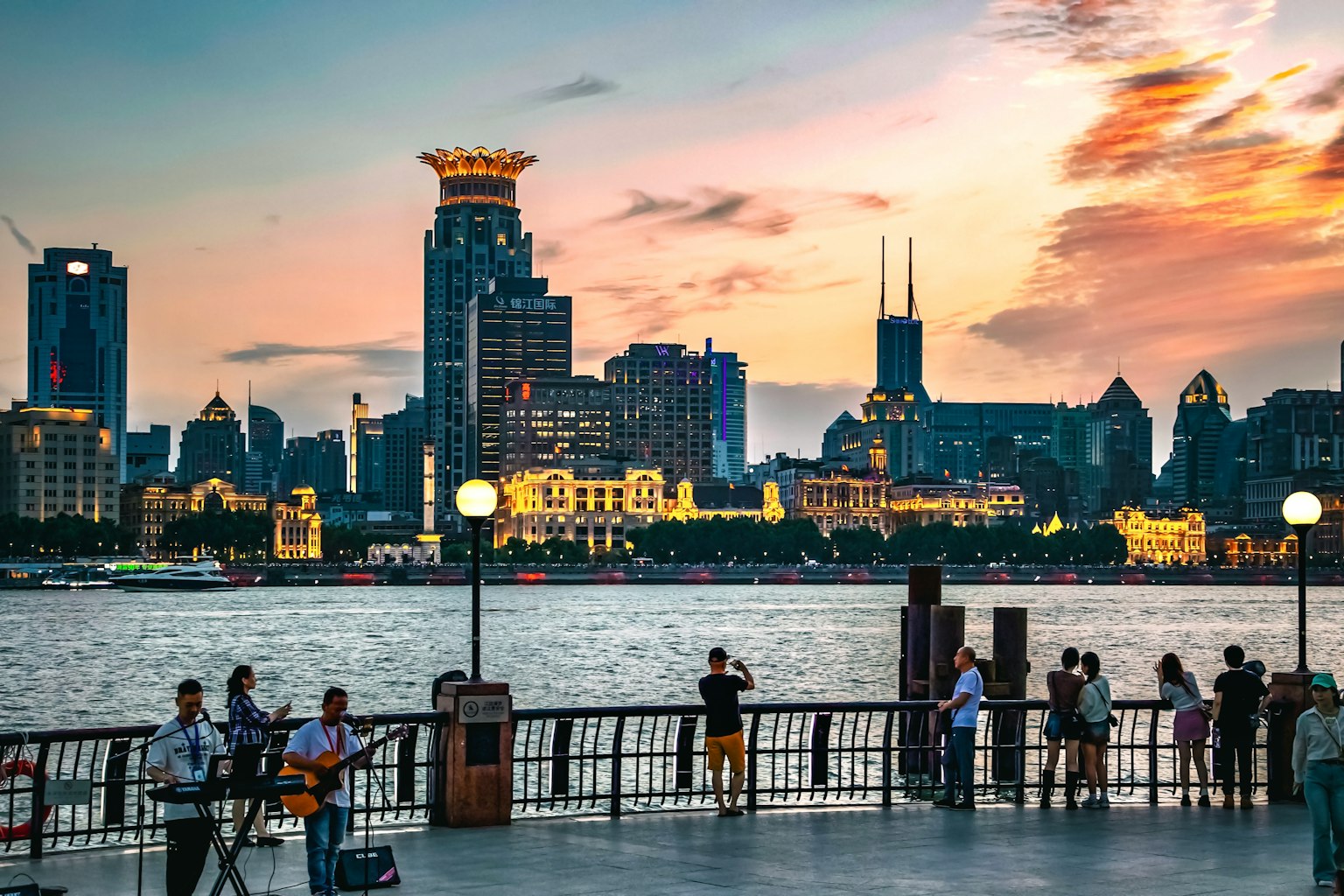 Personnes se tenant le long de la rivière Huangpu avec le skyline de Shanghai au coucher du soleil