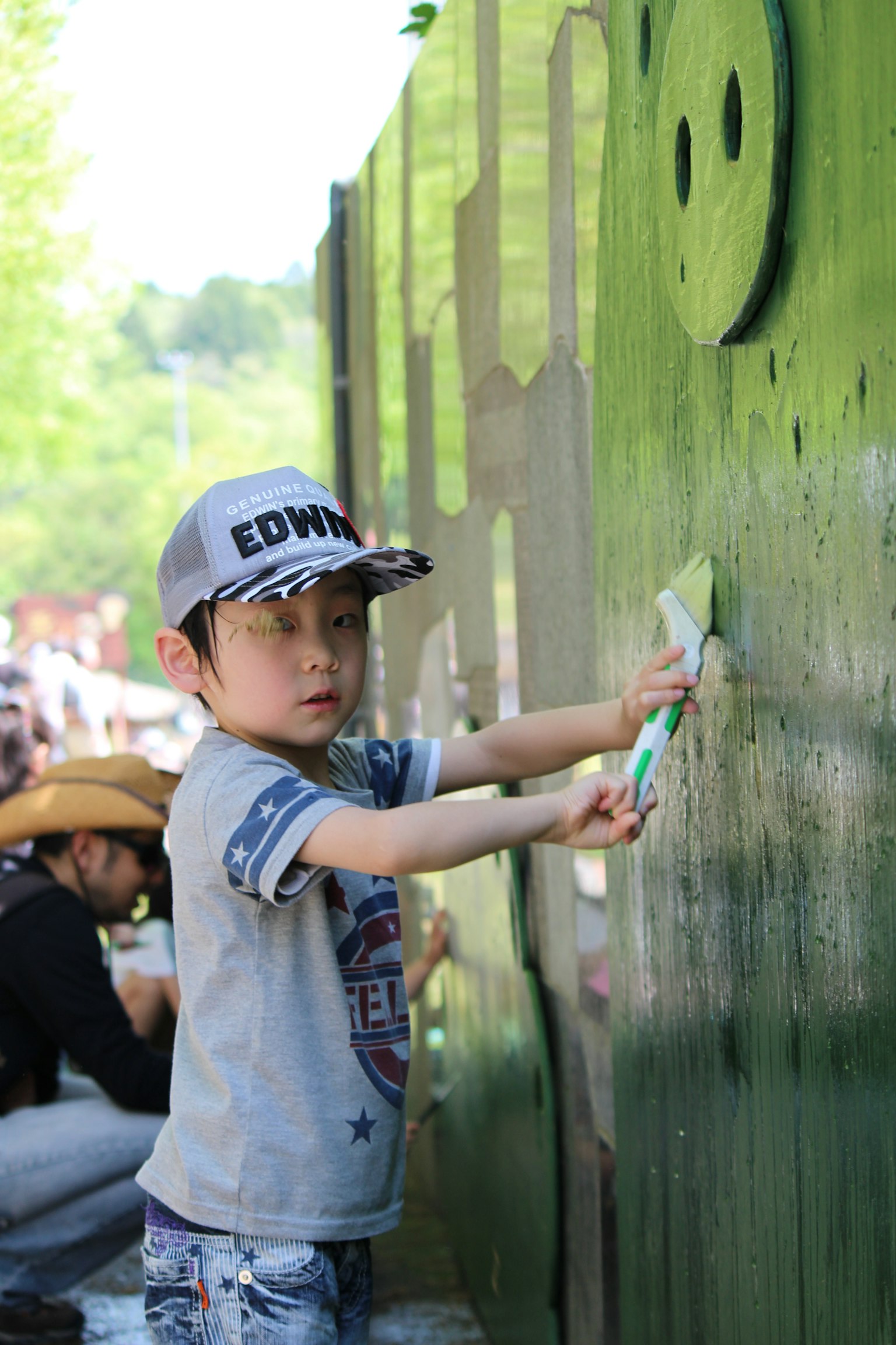 Ein Kind malt eine grüne Wand und trägt eine Mütze