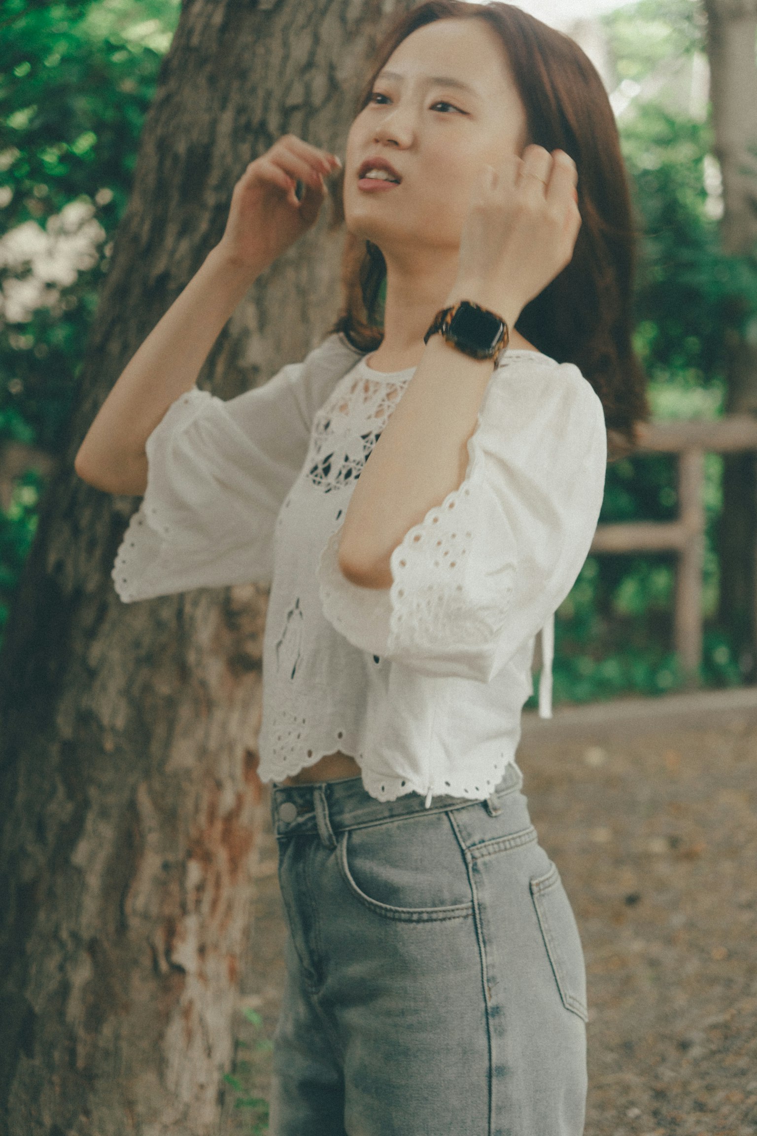 Una mujer con blusa blanca posando cerca de un árbol