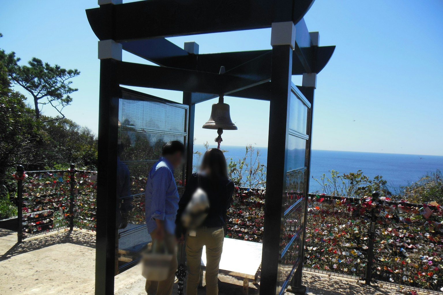 Pareja dentro de una pequeña estructura con una campana con vista al mar azul