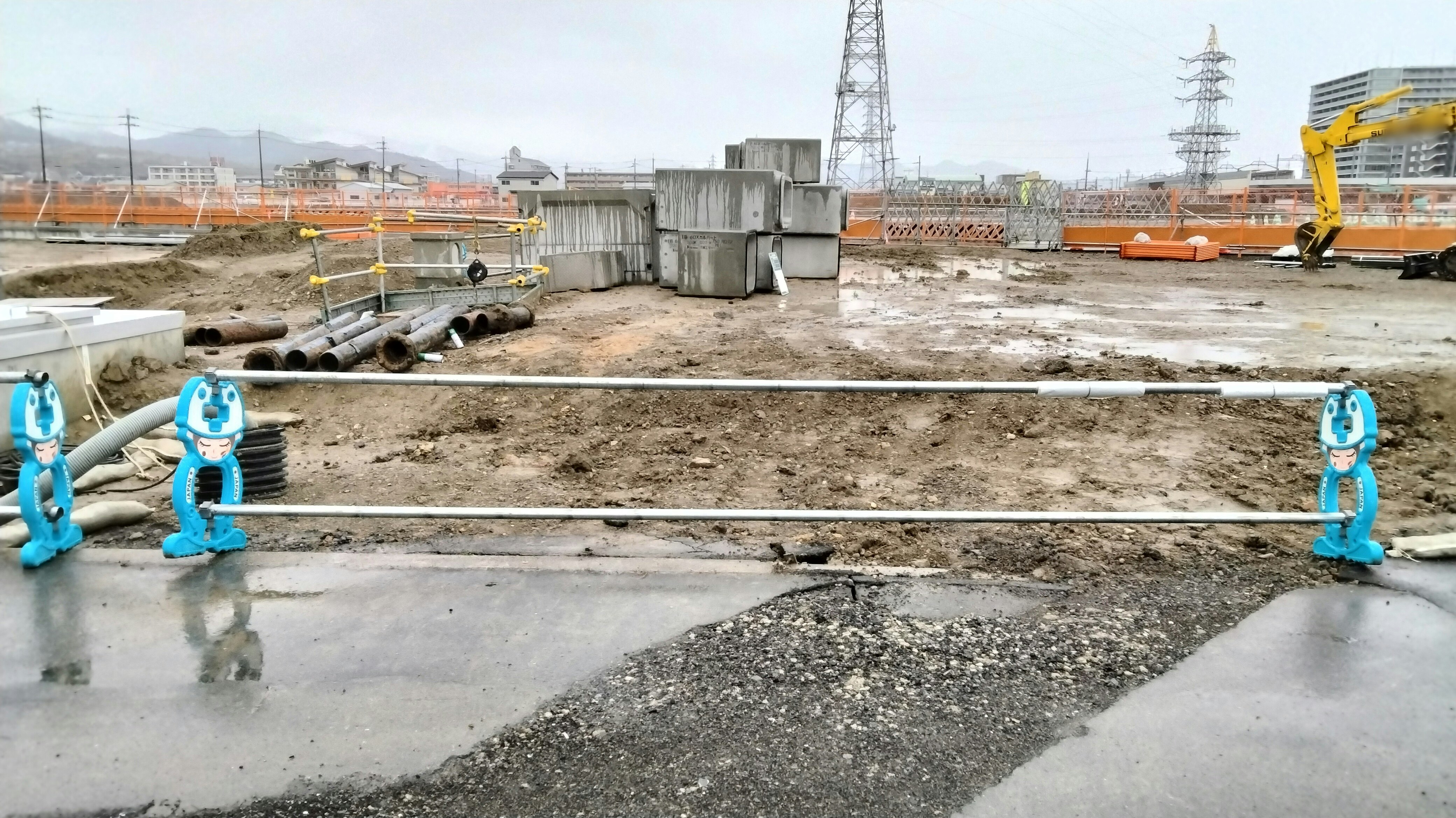 outdoor construction site with heavy machinery and materials along a fence