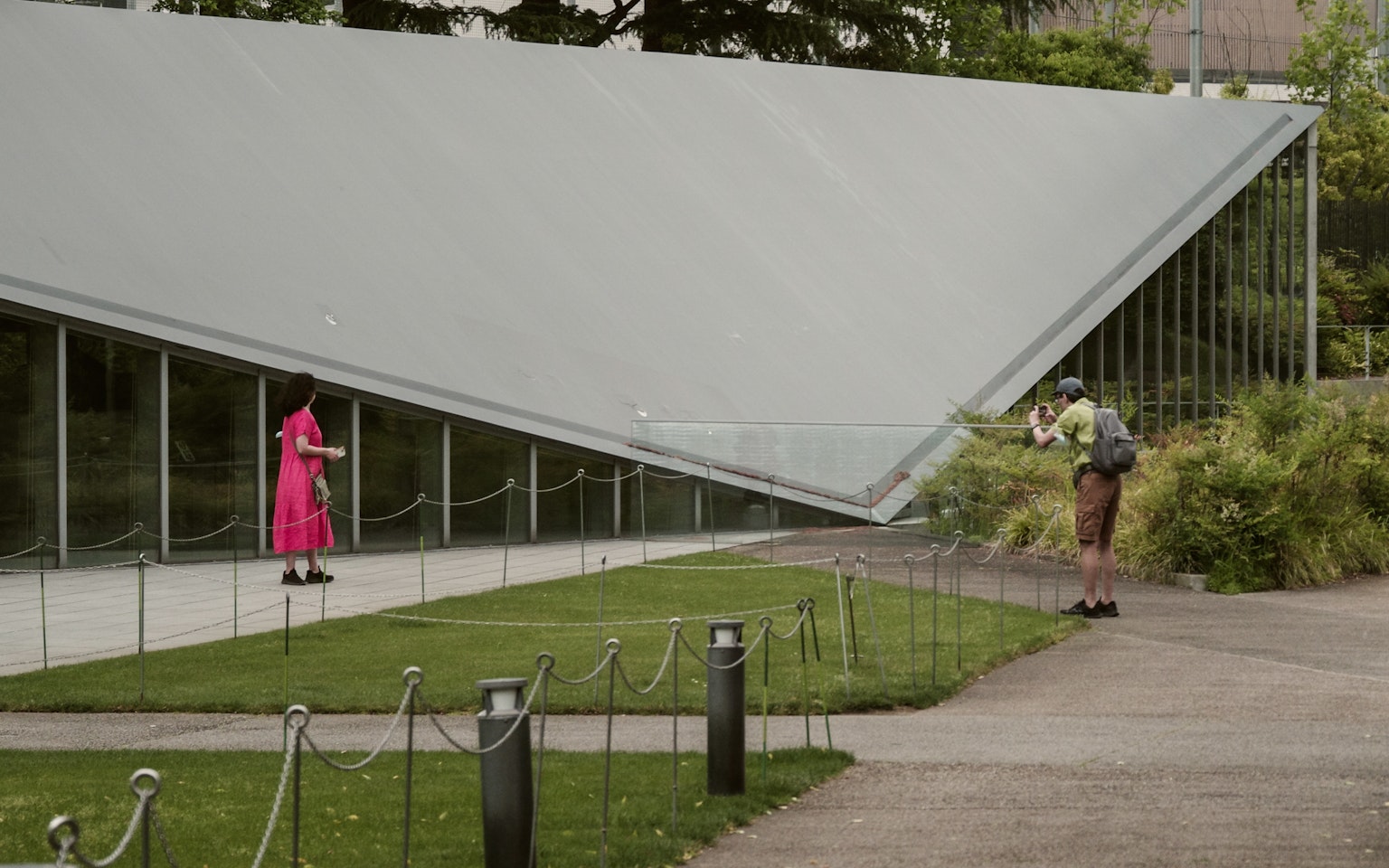 Zwei Personen stehen unter einem modernen Architekturdach mit grünem Gras und Glaswänden