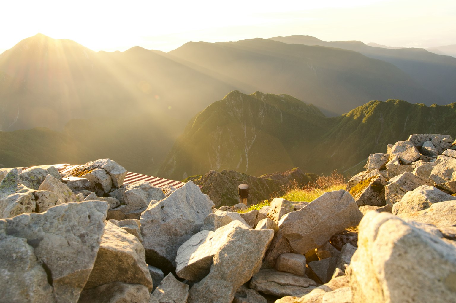Nahaufnahme von Steinen mit Sonnenlicht, das eine Berglandschaft beleuchtet