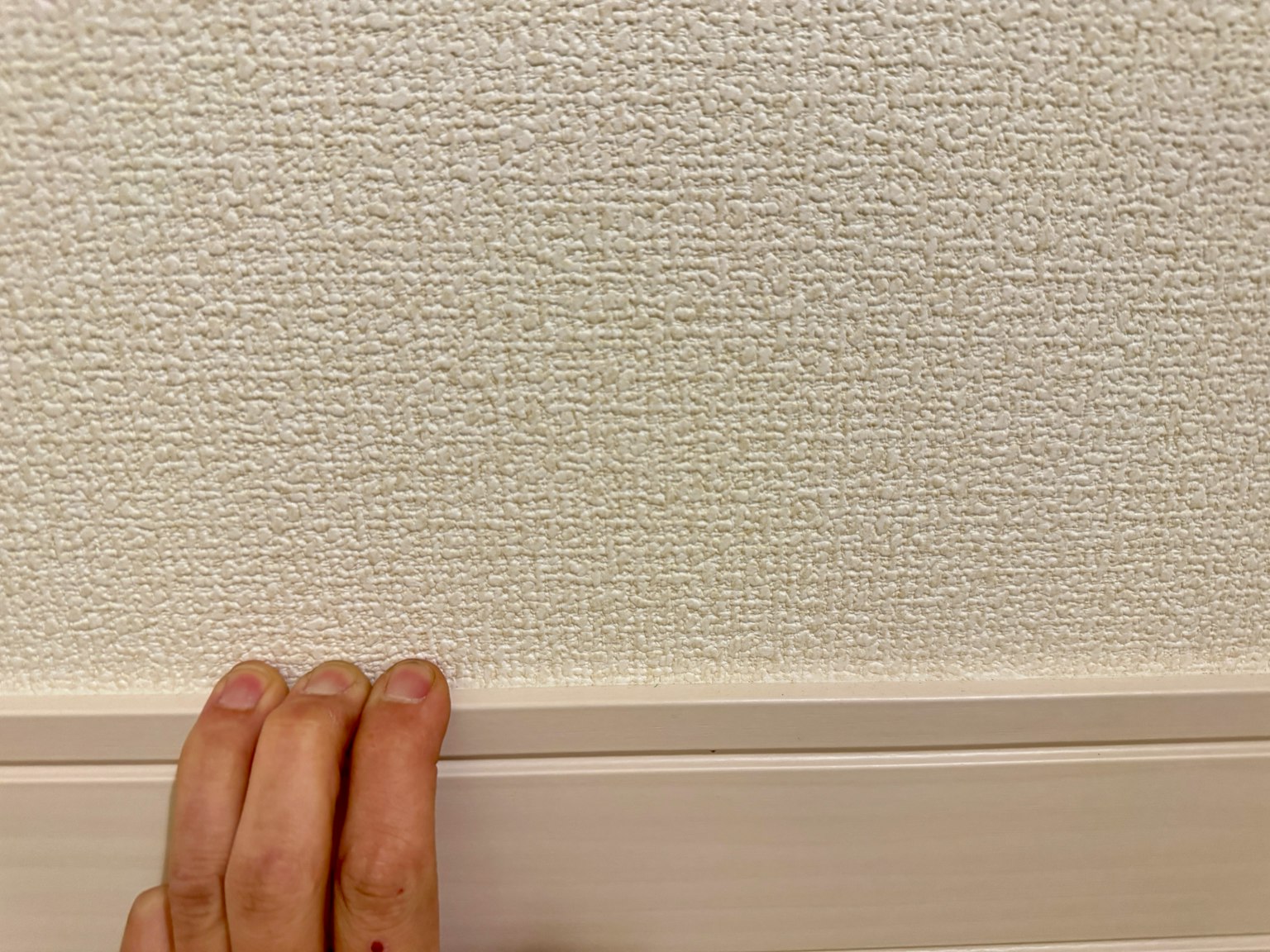 一隻手觸摸著有紋理的白色牆壁，底部有木質裝飾條