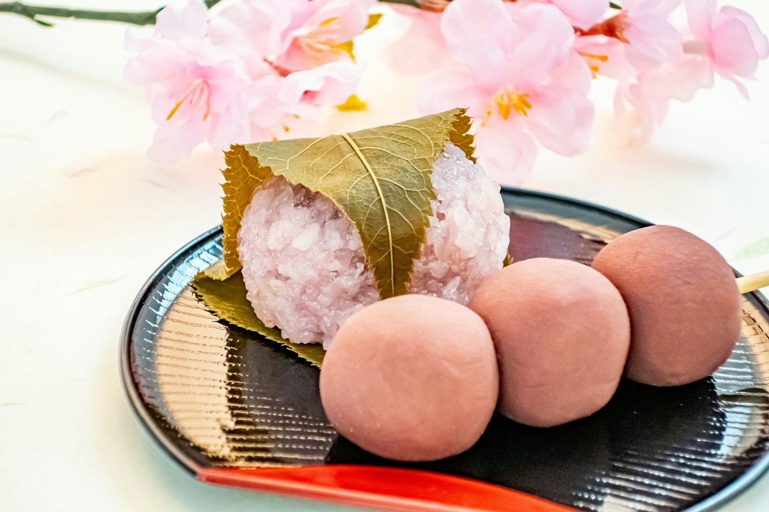 Una hermosa presentación de dulces japoneses que incluye sakura mochi y dango en un plato con flores de cerezo