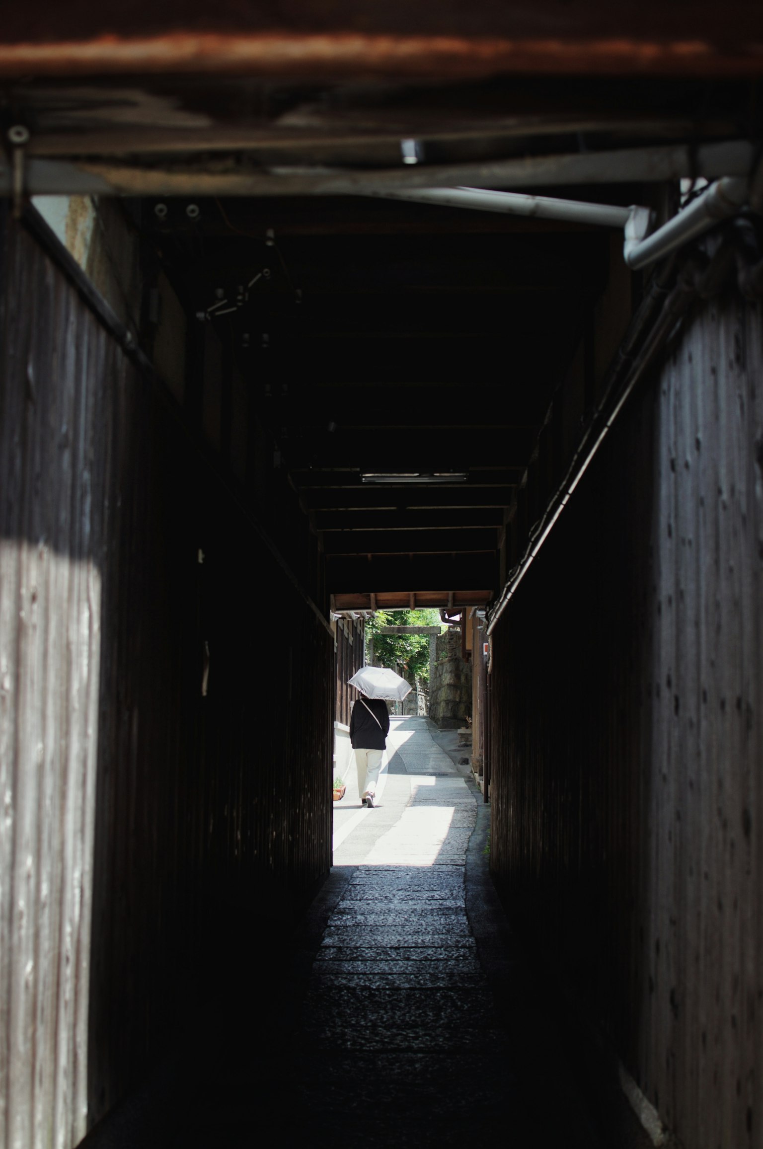 狭い木製の通路の先にいる傘を持った人