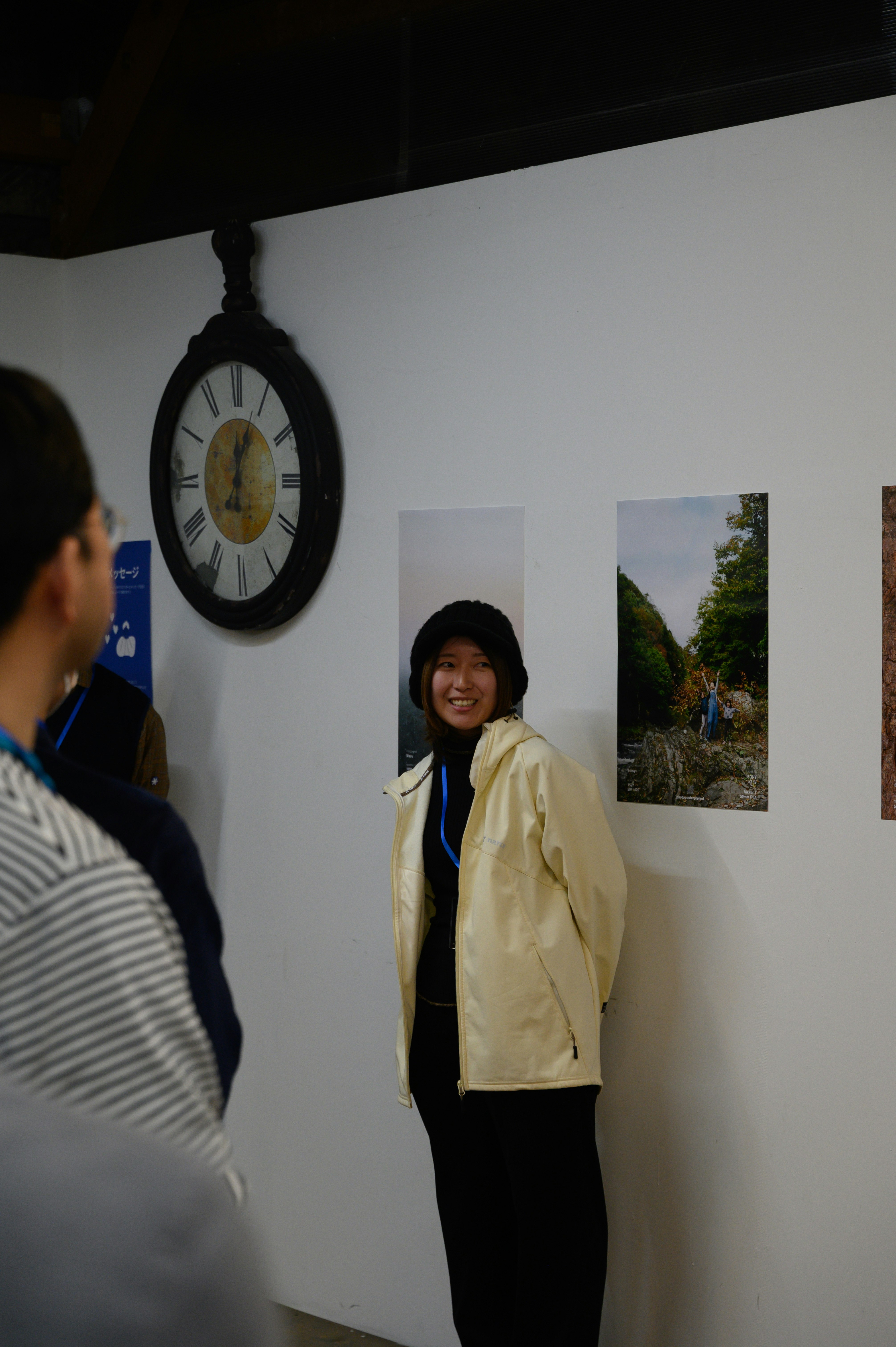 白い壁のギャラリーで展示写真と時計、来場者の人物