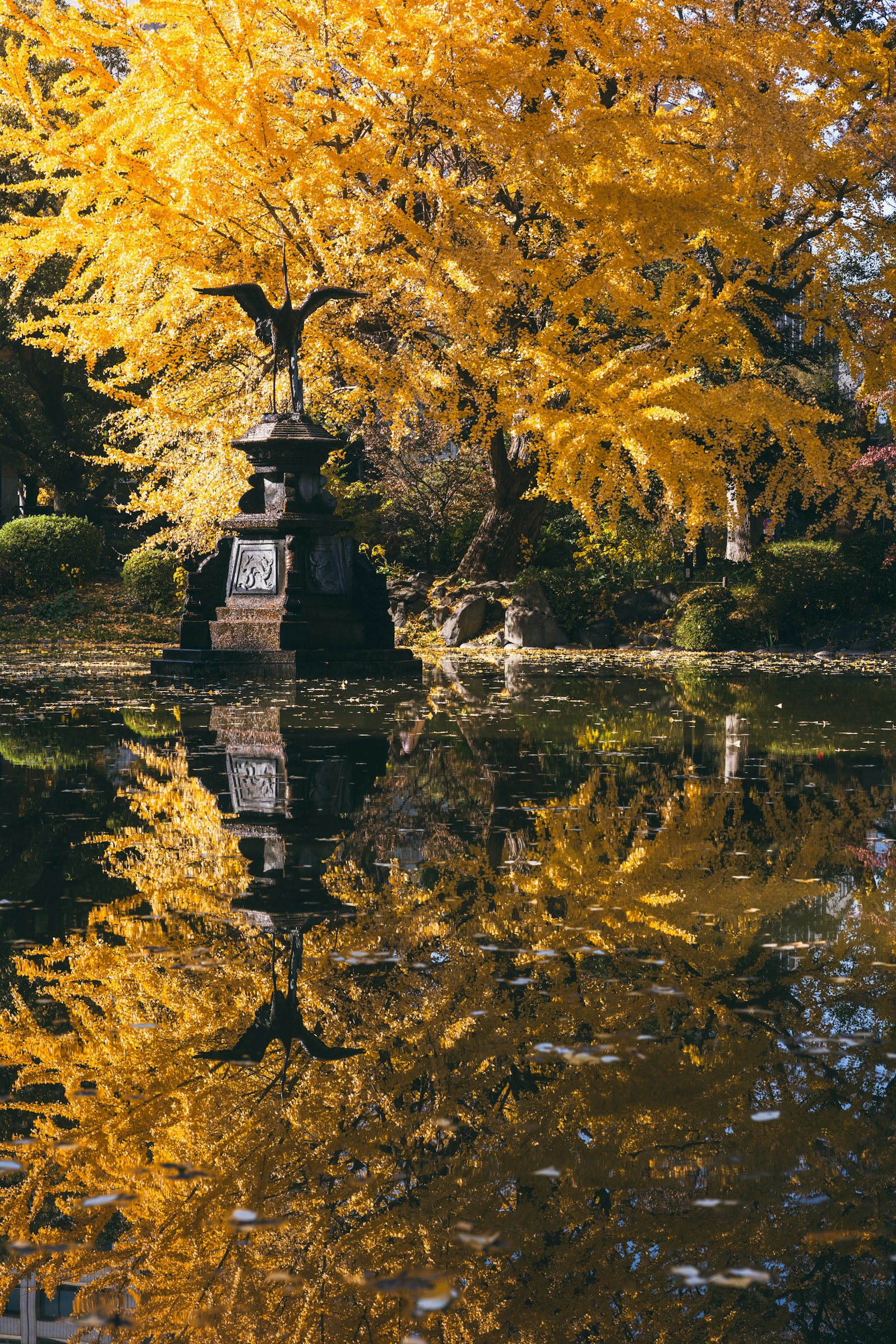 Scena autunnale in un parco con foglie gialle e una scultura riflessa nell'acqua
