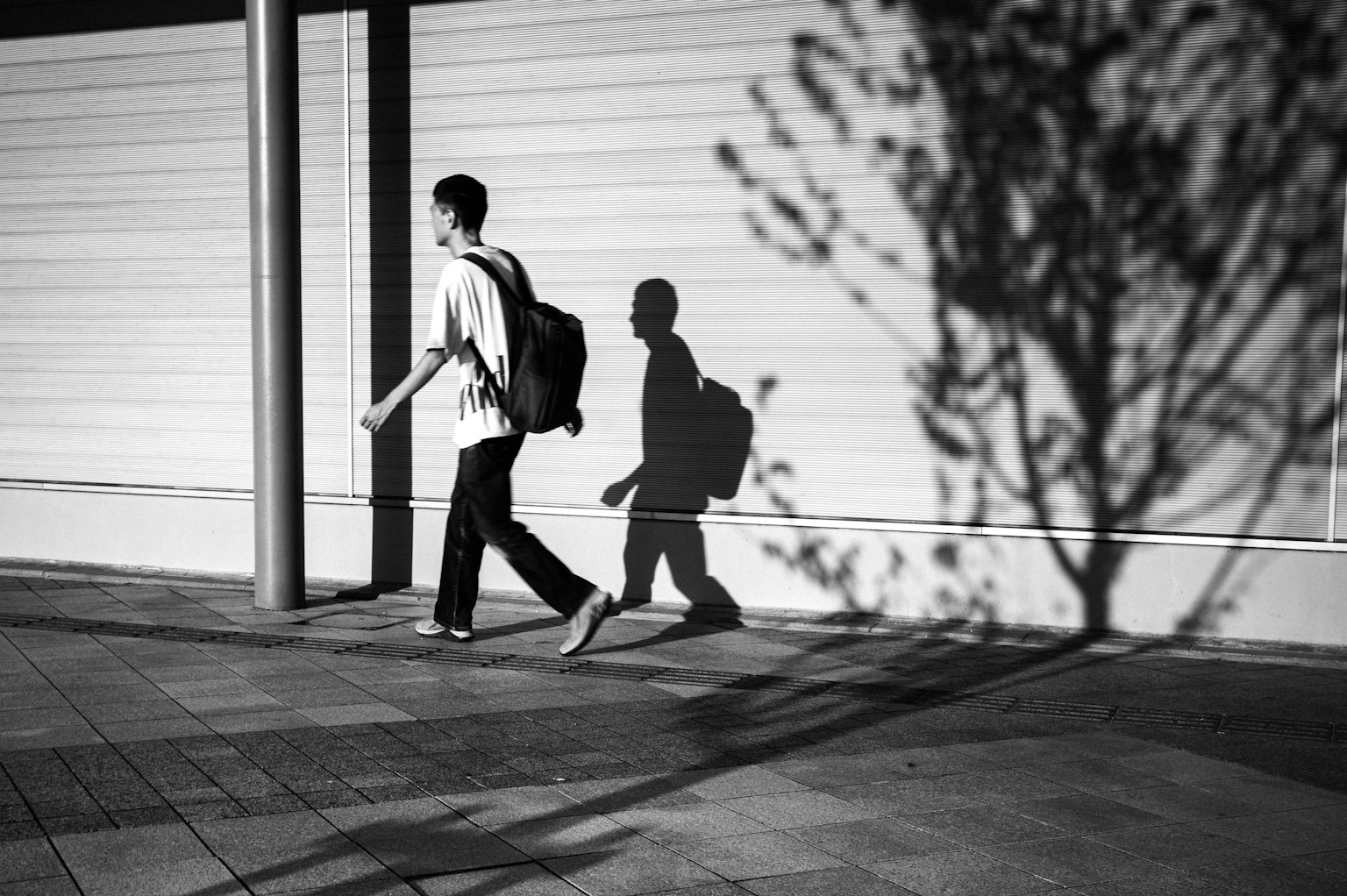 A young person walking in a black and white urban setting with a shadow cast on the ground