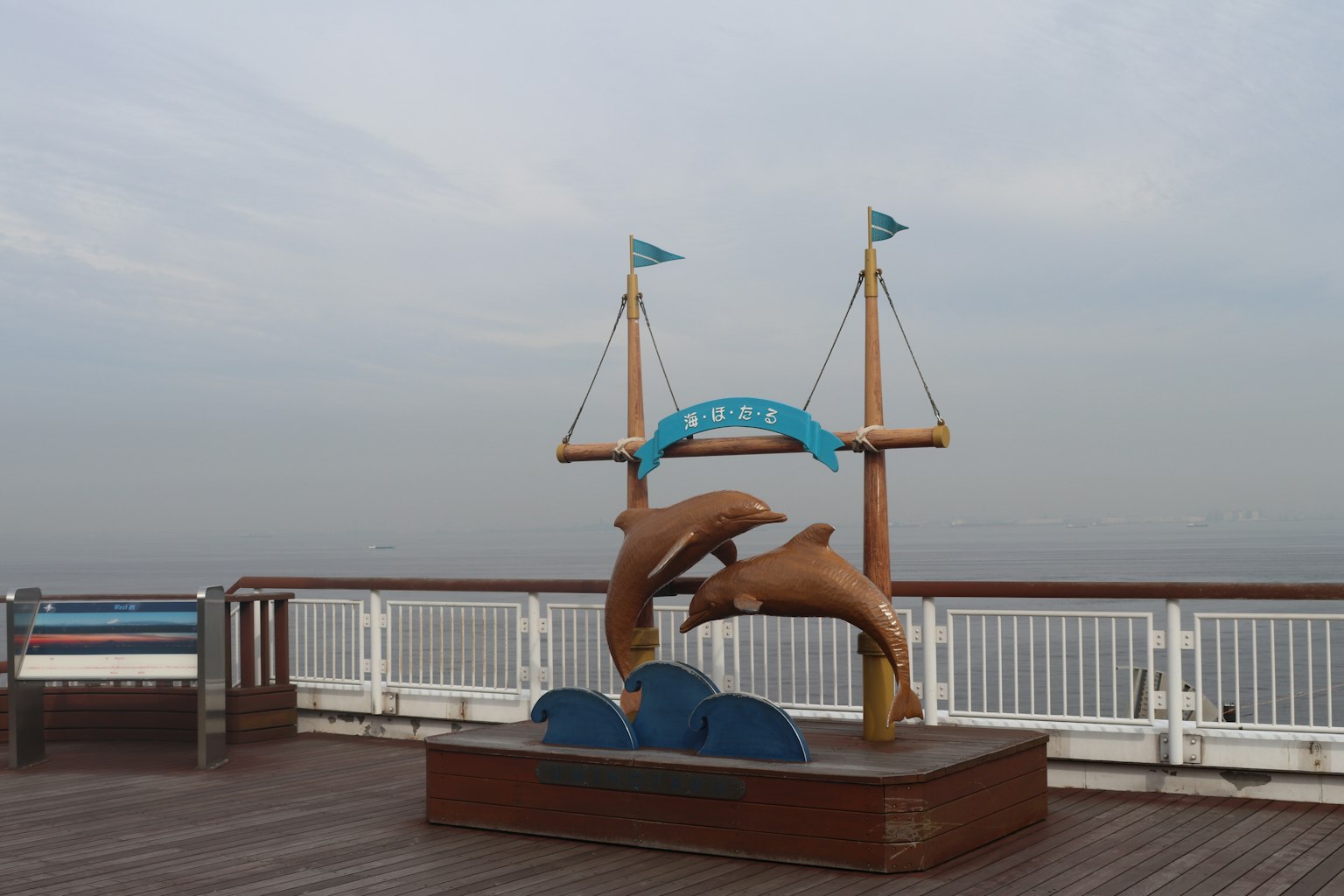 海洋附近甲板上的海豚雕塑和藍色旗幟