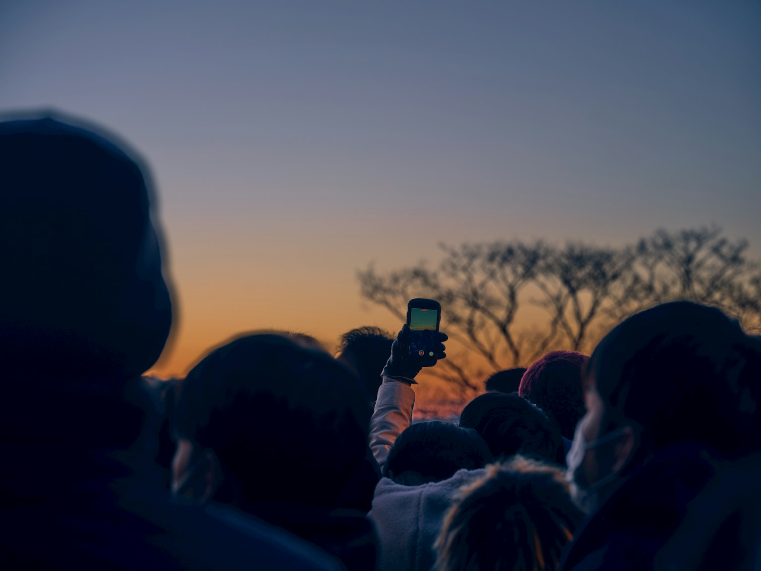 Multitud de personas con un teléfono inteligente contra un fondo de atardecer