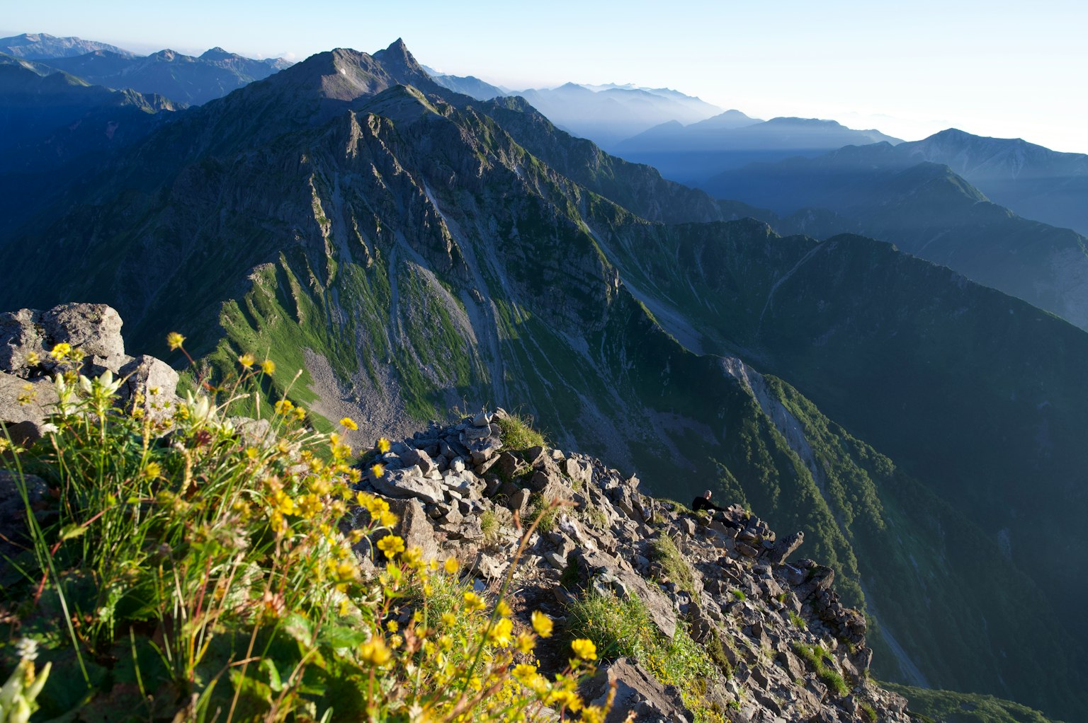 Beeindruckende Aussicht von einem Berggipfel mit grünem Gras und gelben Blumen im Vordergrund