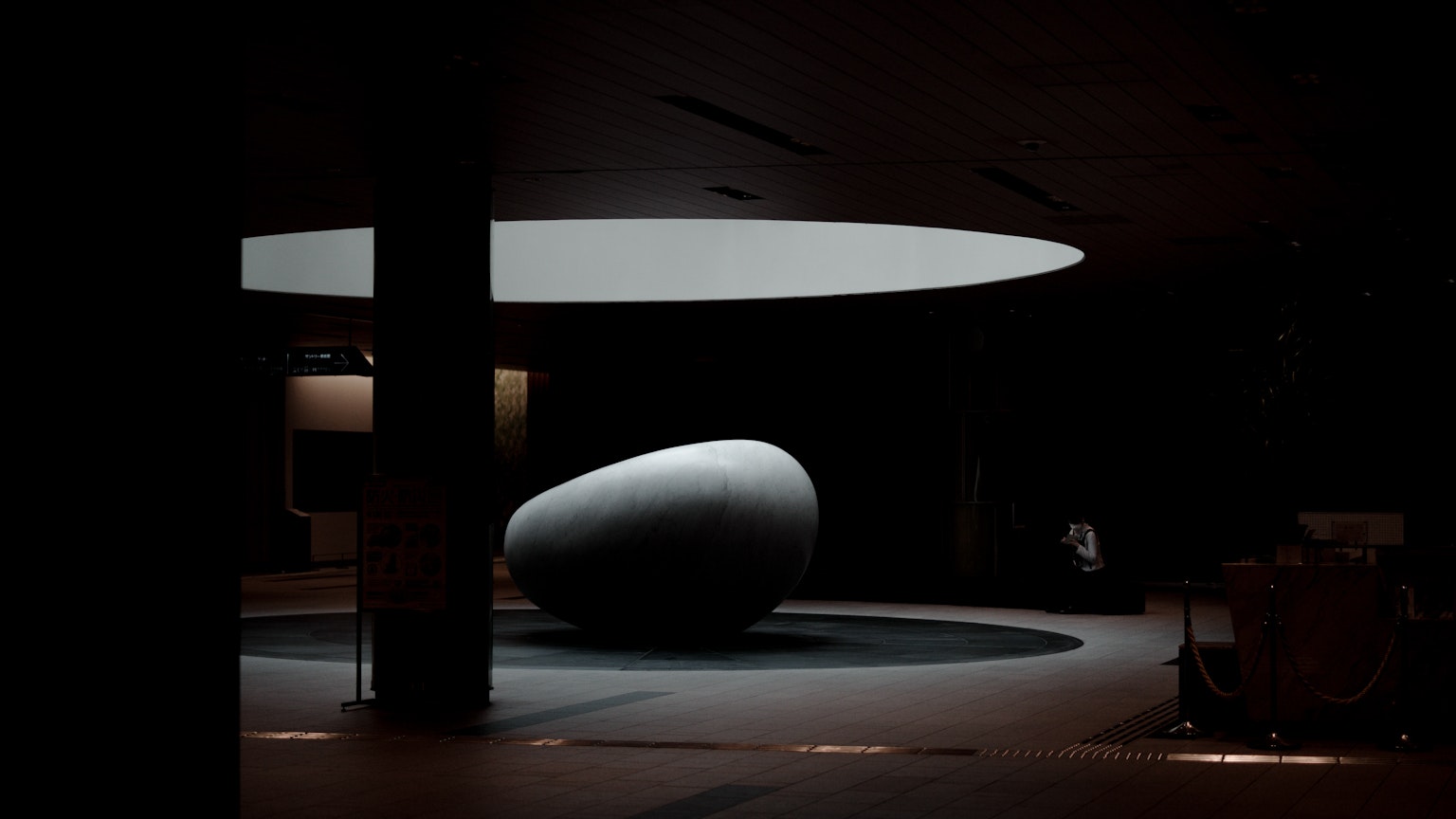 Una escultura en forma de huevo iluminada en un espacio oscuro con una luz circular arriba