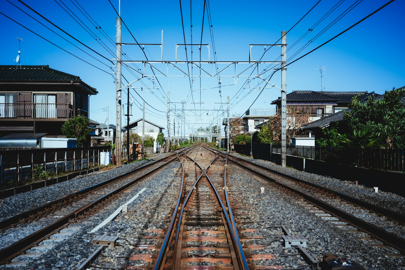 รางรถไฟที่ยาวเหยียดไปในระยะไกลใต้ท้องฟ้าสีฟ้าสดใสพร้อมบ้านใกล้เคียง