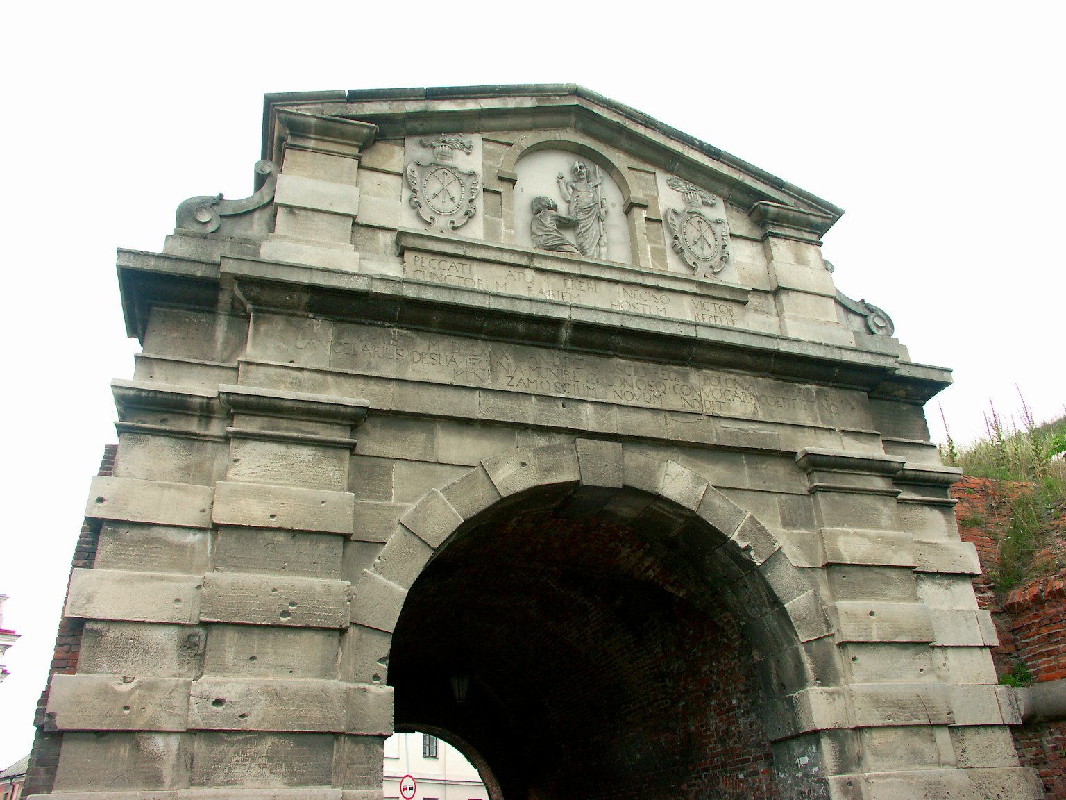 Ruinas de un antiguo arco de piedra con escudos tallados en la parte superior