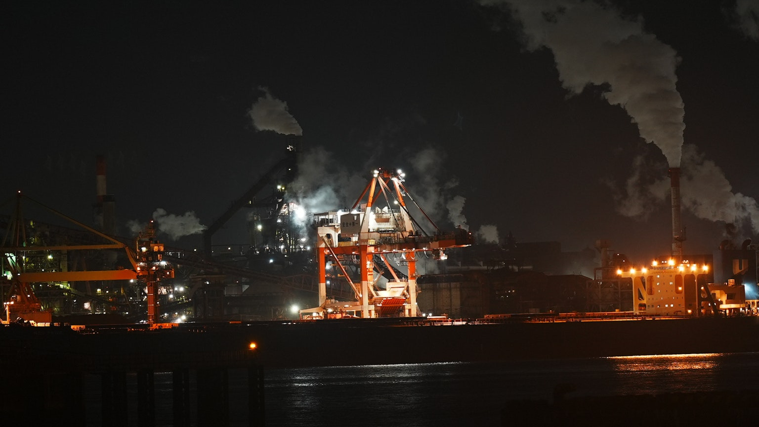 Zone industrielle nocturne avec grues et fumée