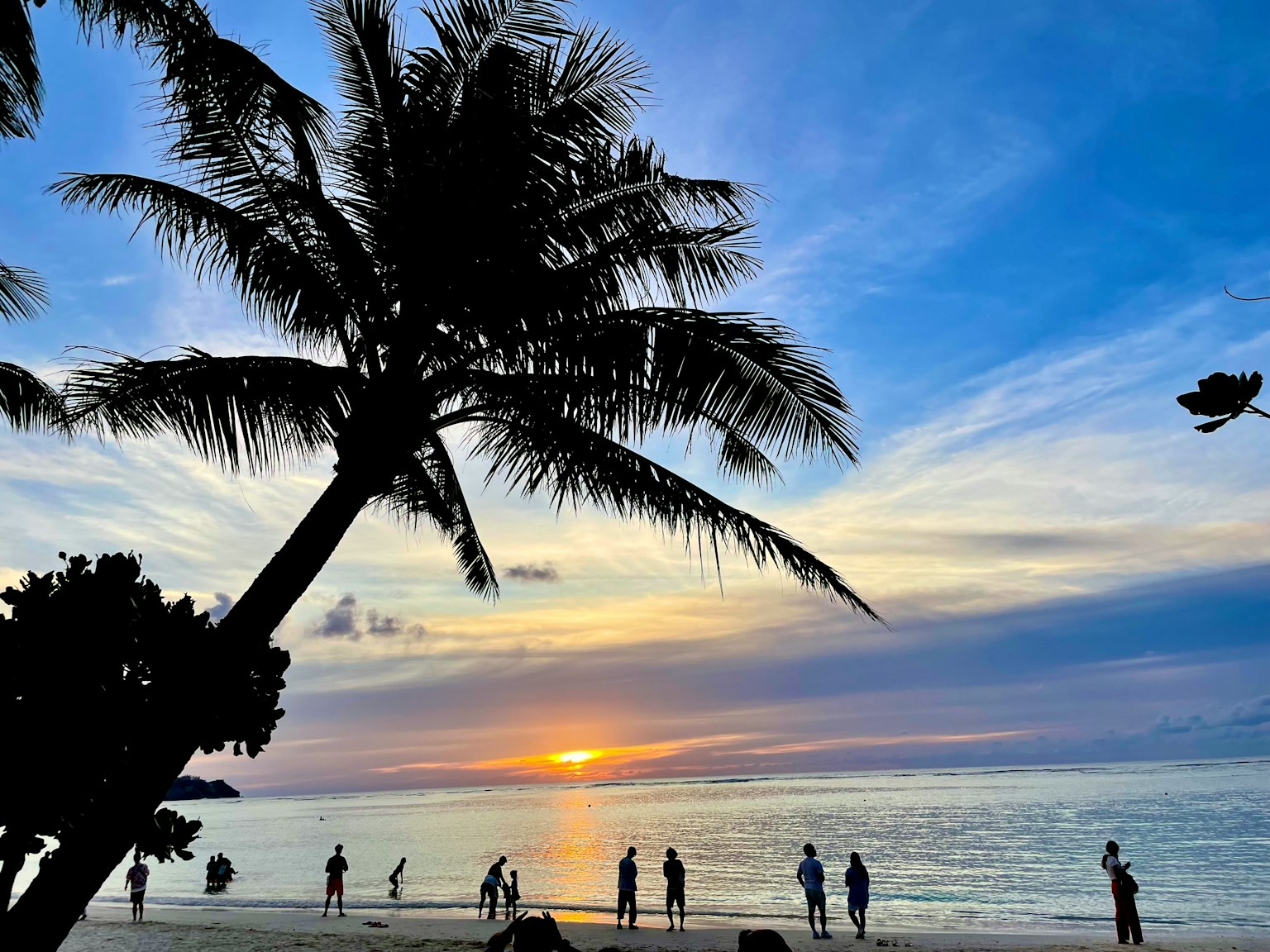 Silhouette von Palmen mit Menschen, die am Strand bei Sonnenuntergang spielen