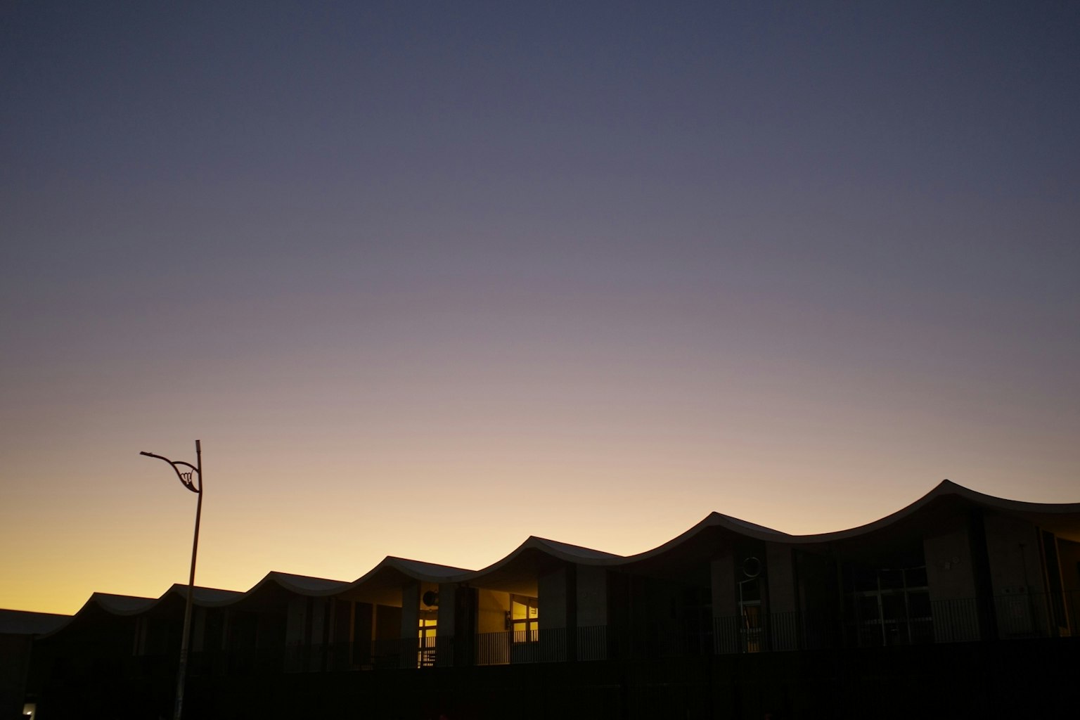 夕暮れ時の波状の屋根を持つ建物のシルエット