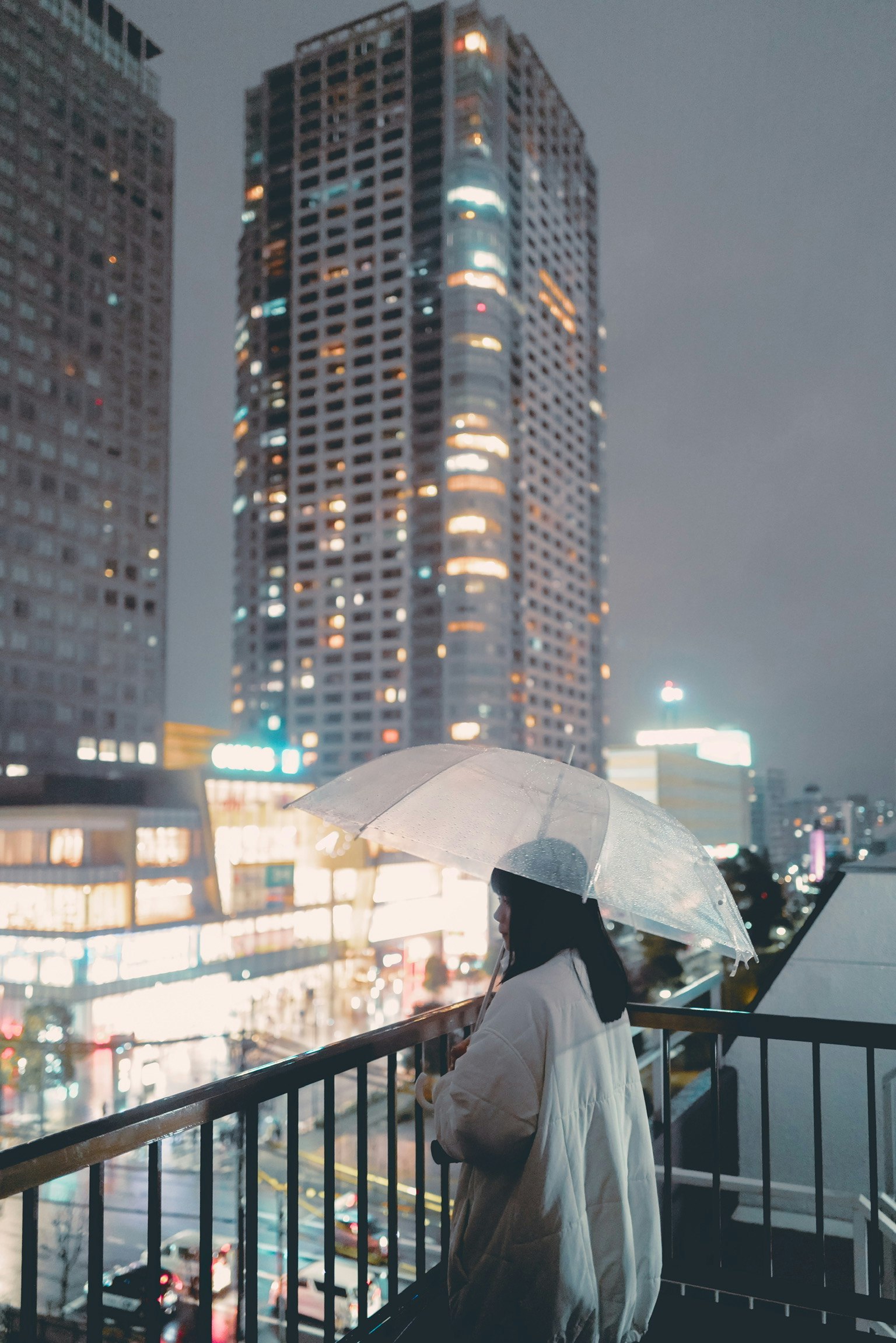 女性手持雨傘俯瞰夜晚的城市天際線，建築物燈光閃爍