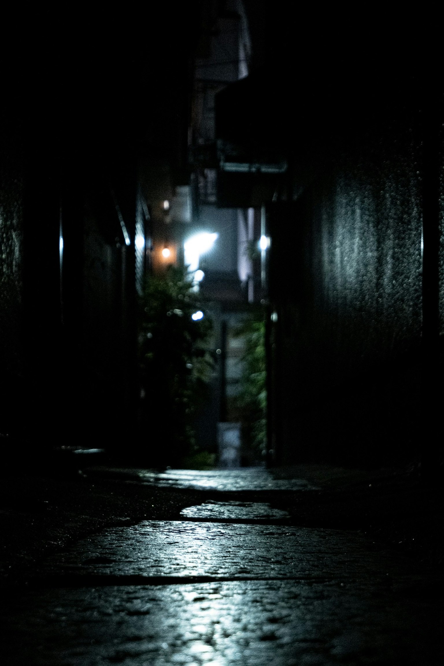 暗い路地の先に明かりが見える湿った石畳