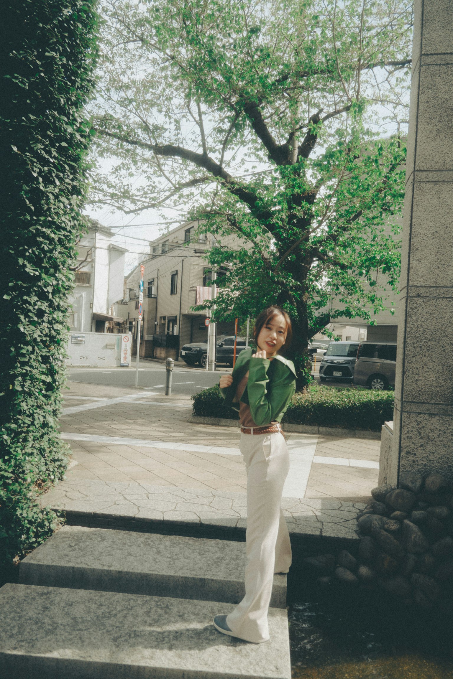 Une femme se tenant devant un arbre vert portant un pantalon clair et un haut vert