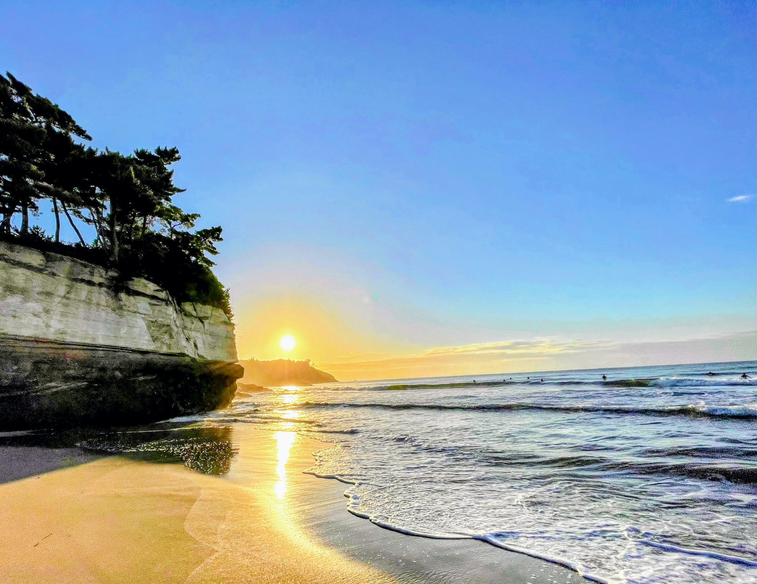 Bellissimo tramonto sulla spiaggia con onde che si infrangono sulla sabbia e alberi sulla scogliera
