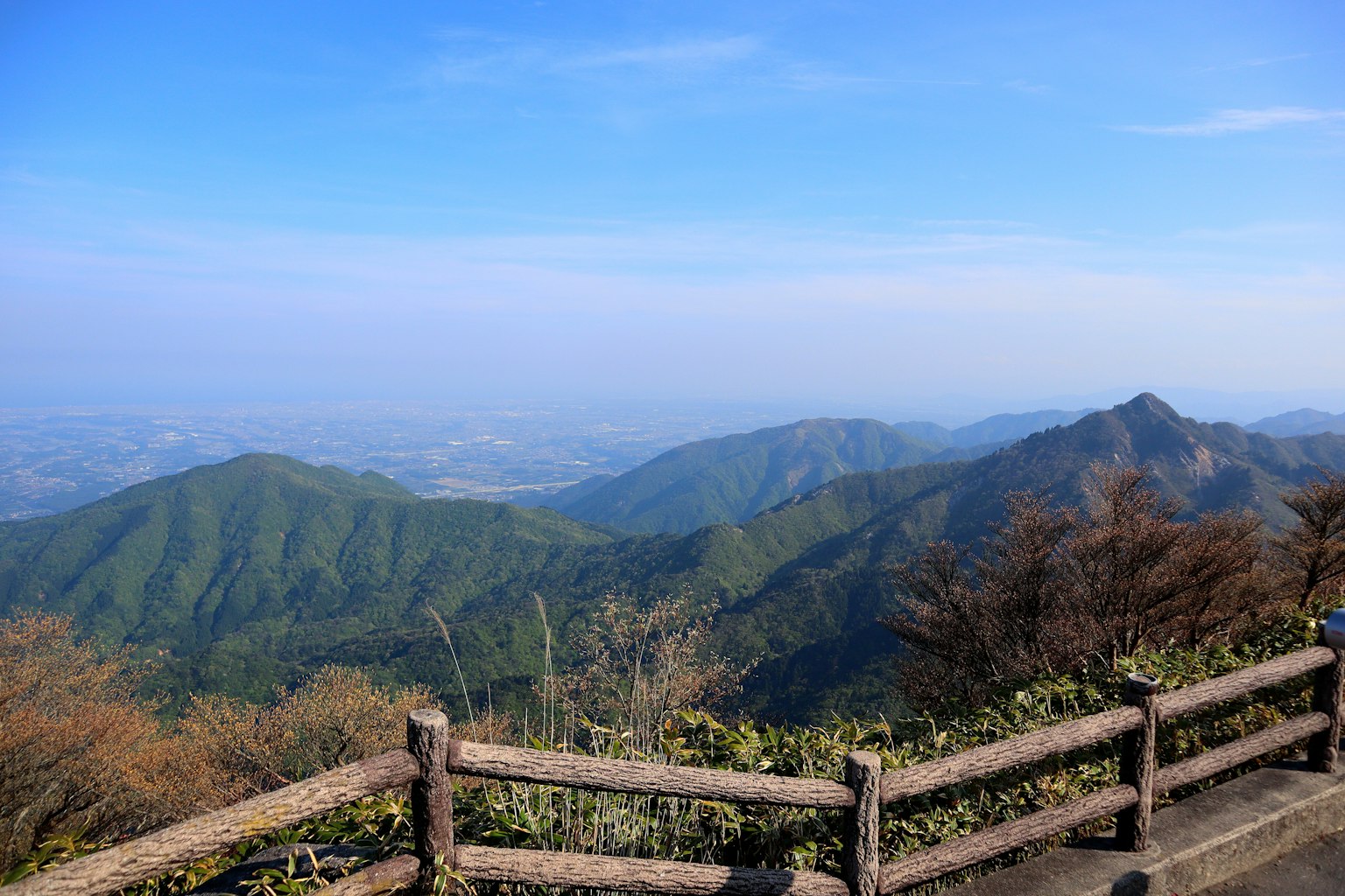 Pemandangan pegunungan hijau di bawah langit biru dengan pagar kayu