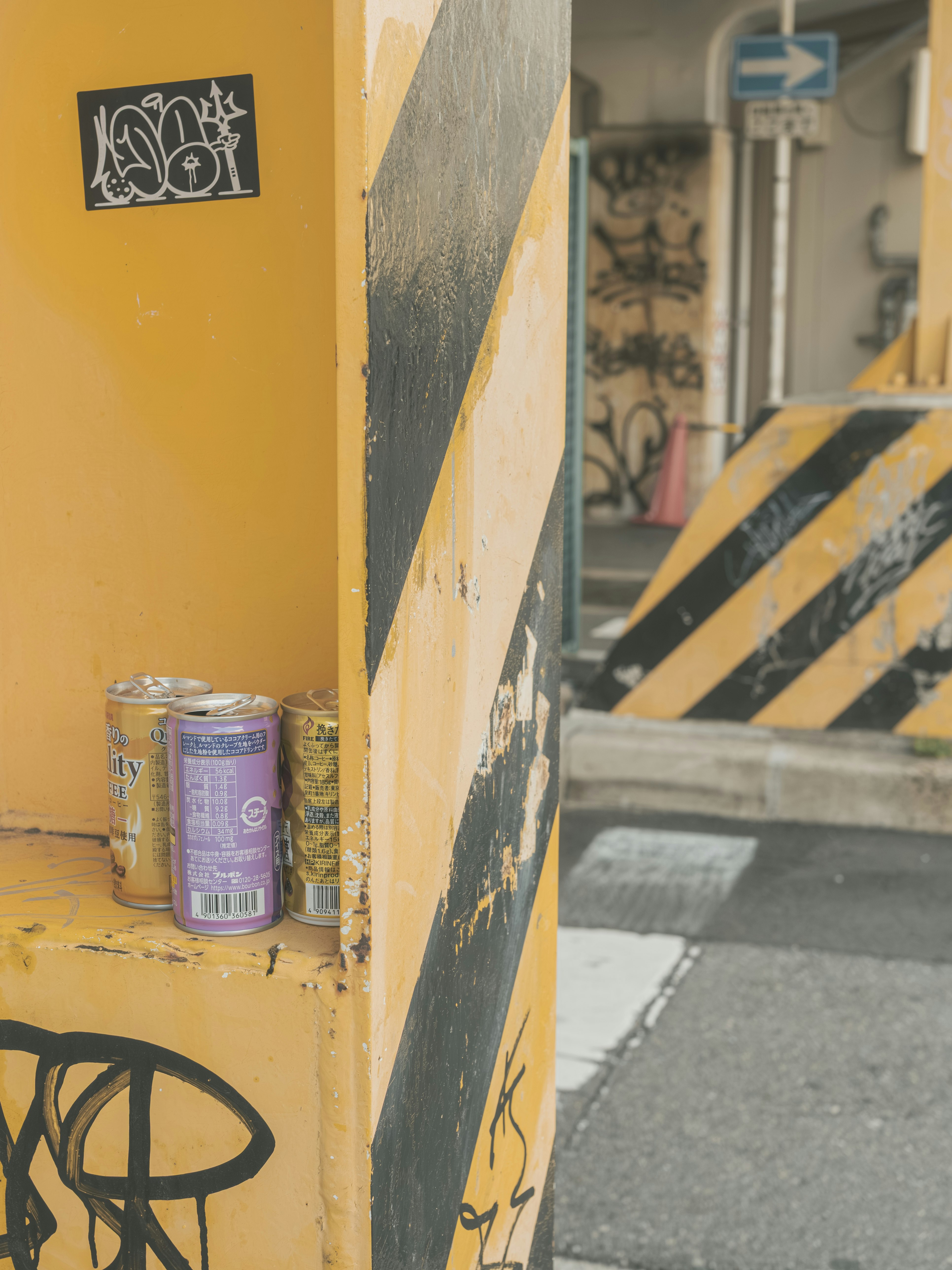 黄色い壁の前に置かれた塗料缶と落書きのある路地の一角