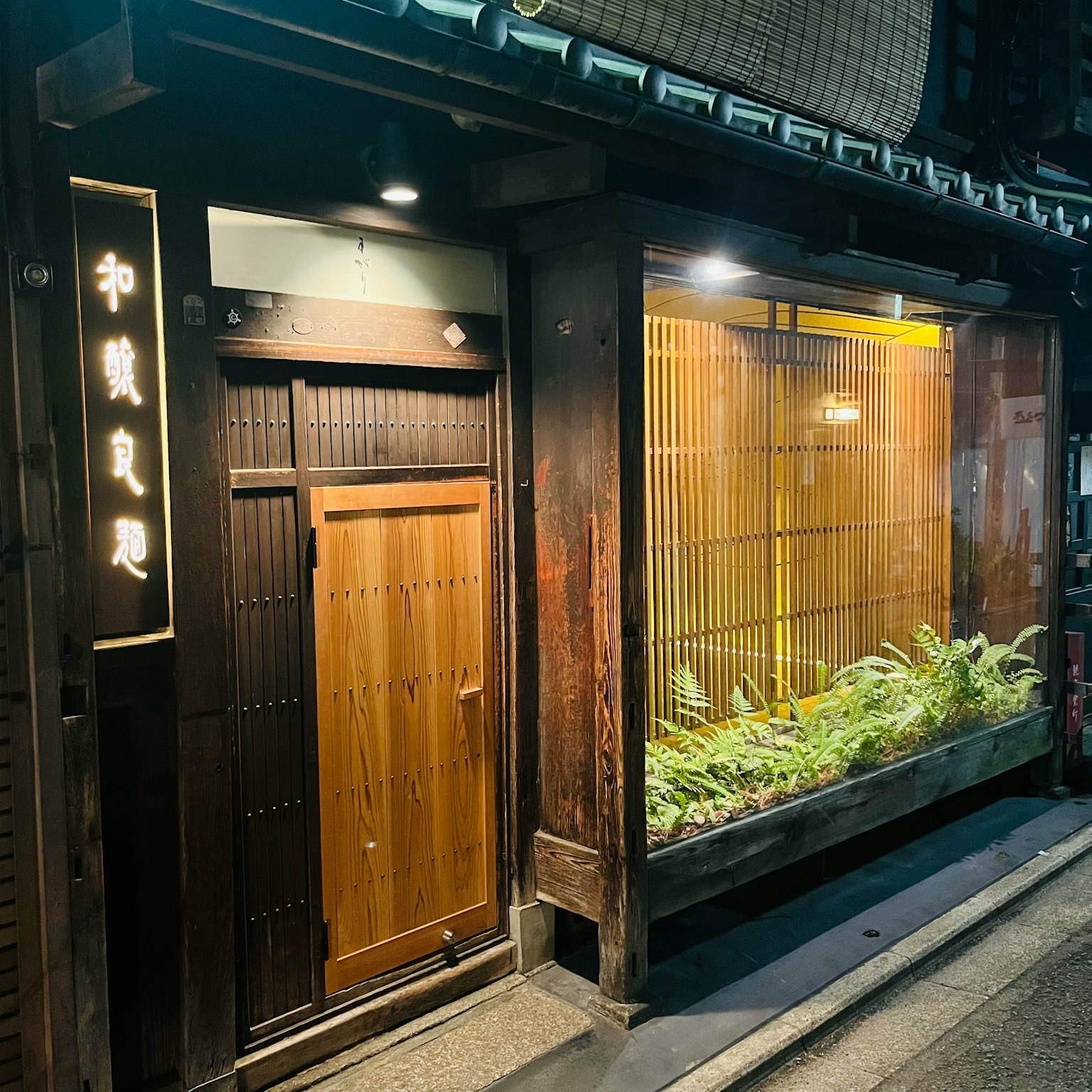 Esterno di un ristorante giapponese tradizionale con illuminazione notturna e piante verdi
