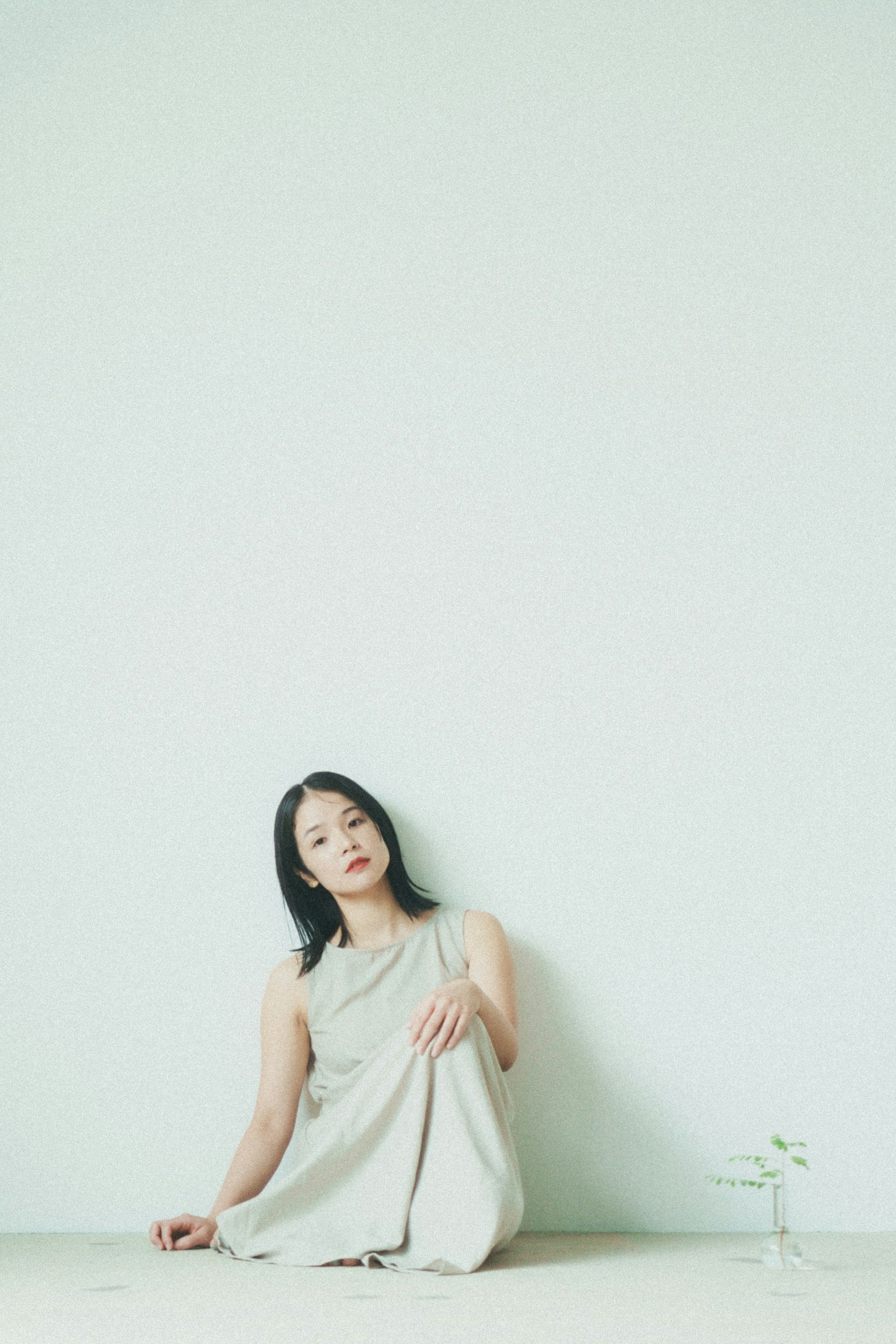 A woman sitting against a white wall with a calm expression