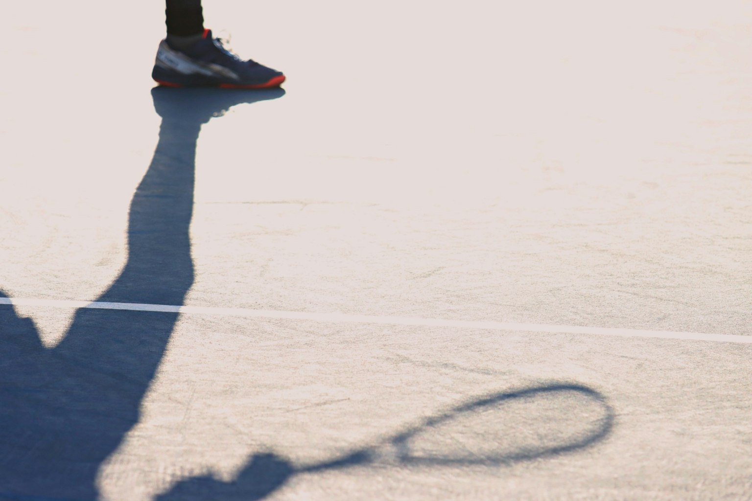 Bayangan raket tenis yang dipegang oleh pemain di lapangan dengan sepatu terlihat