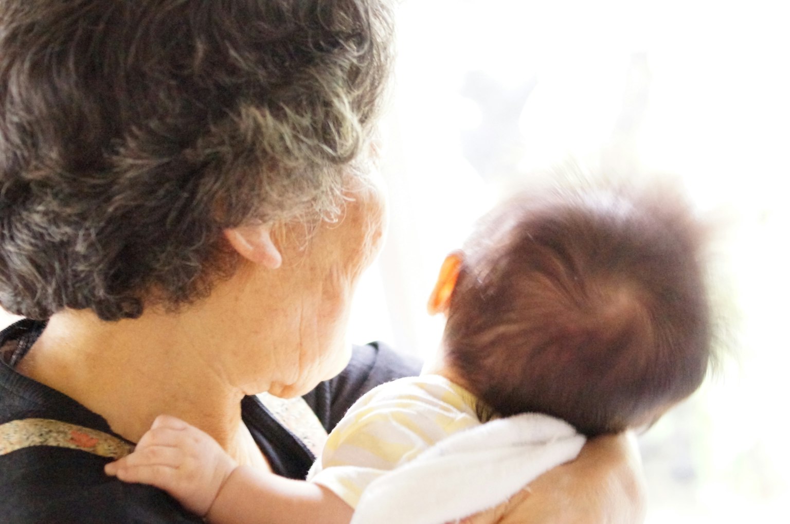 Una mujer anciana sosteniendo a un bebé mirando por la ventana