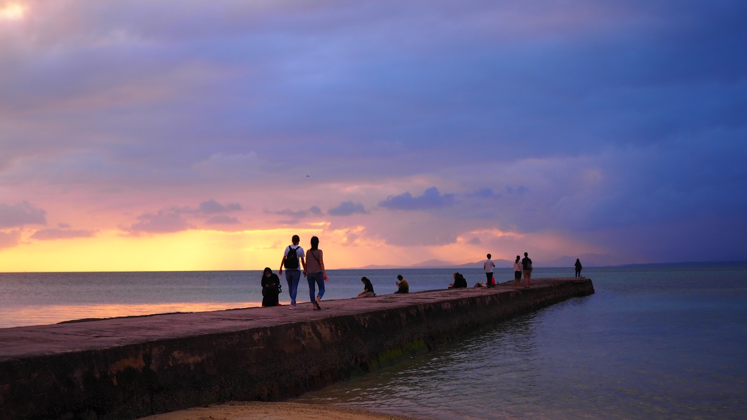 Silhouettes of people walking on a pier during sunset