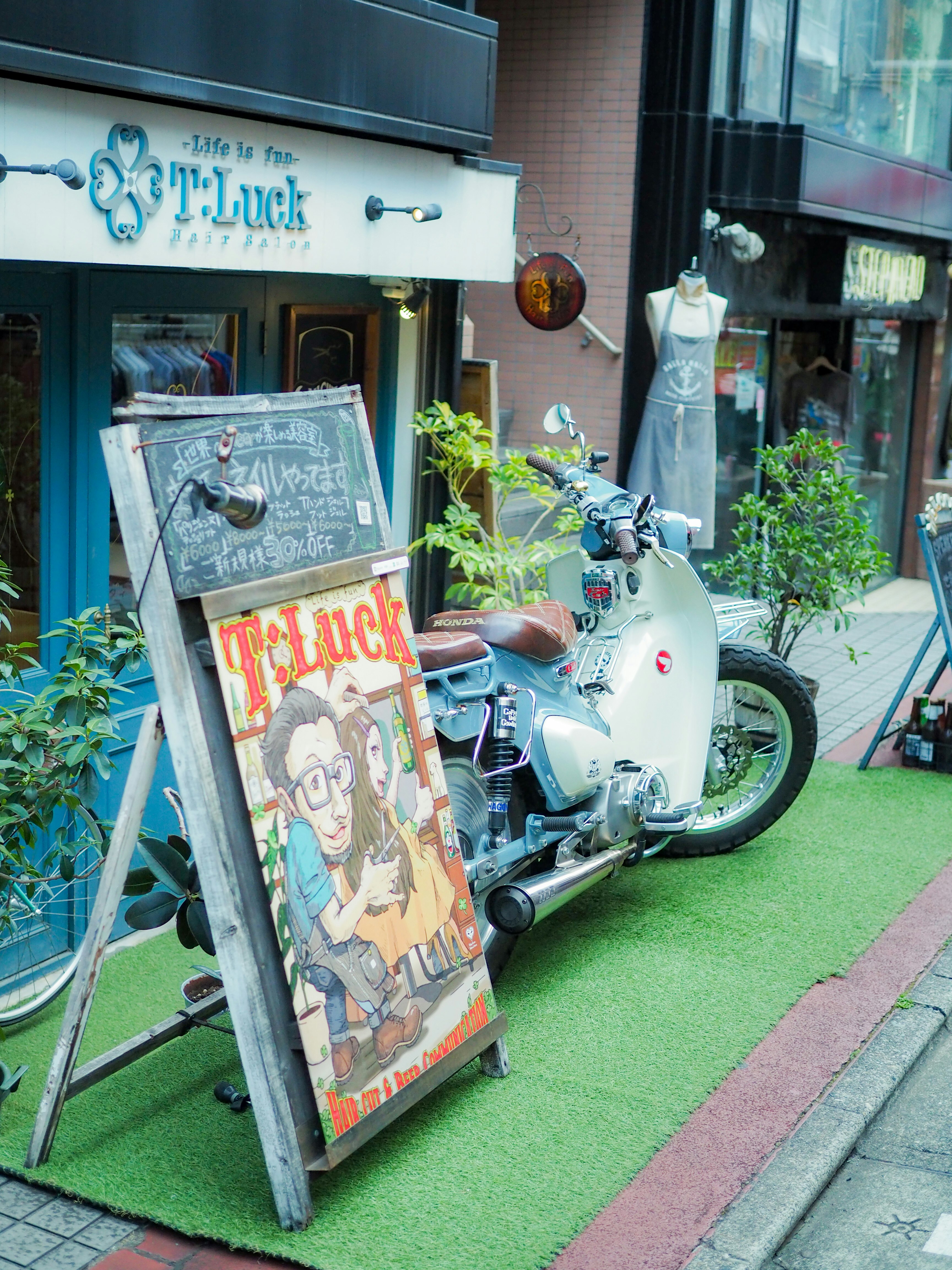 店先に並ぶ観葉植物と白いスクーターのある小さな路地の看板