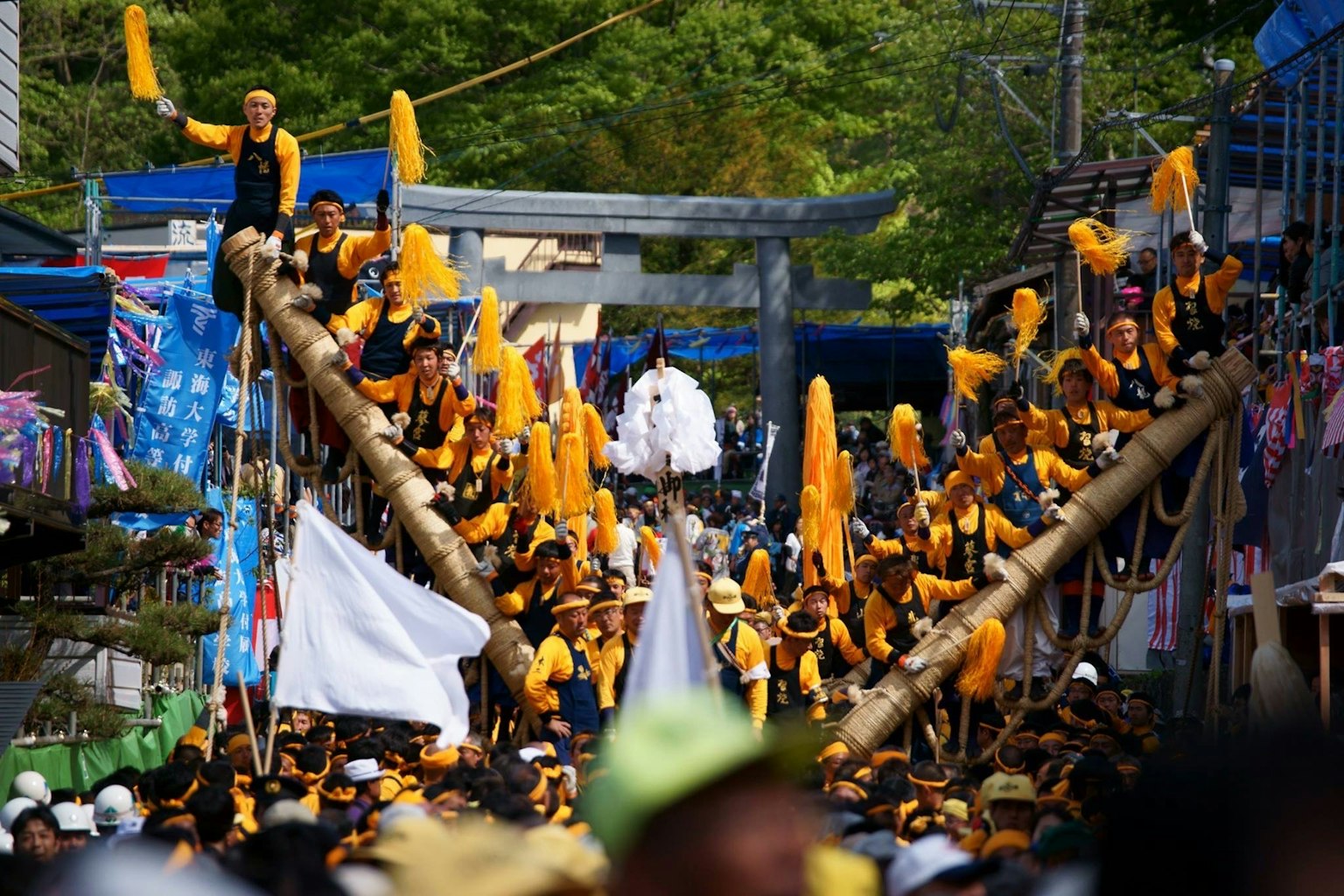 Foule soulevant des poteaux en bambou lors d'un festival vibrant avec des participants en tenue jaune