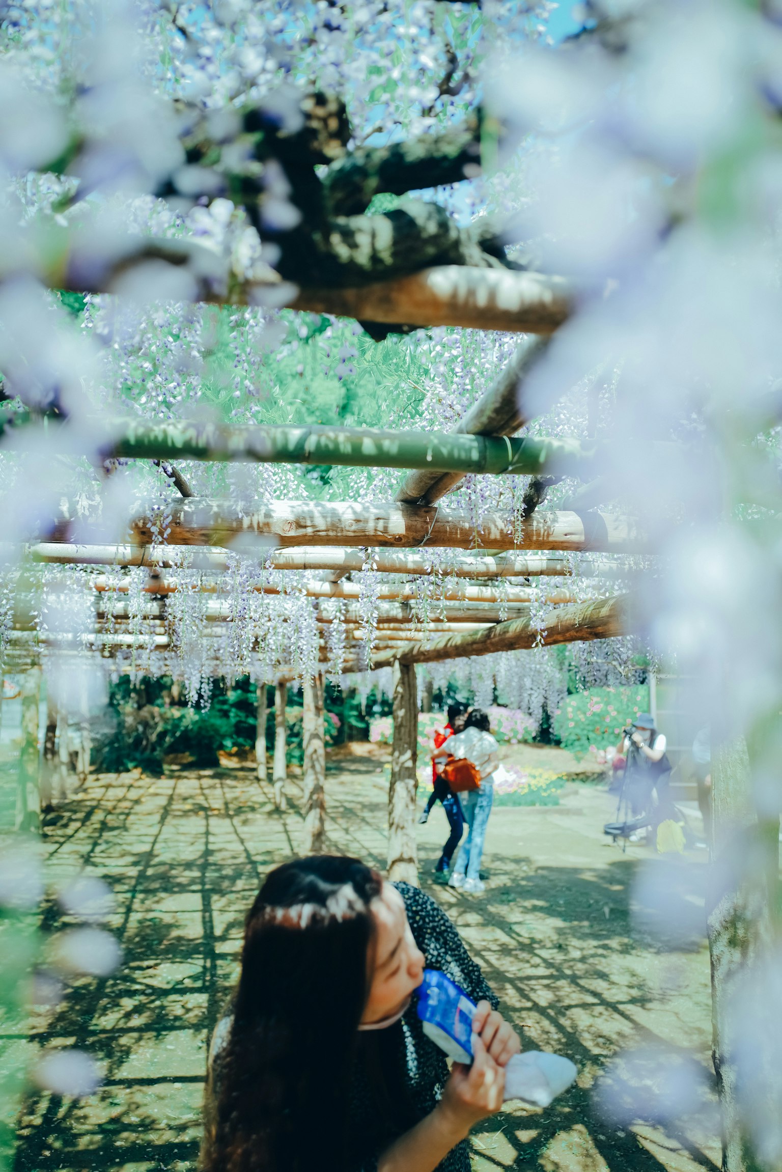 Una donna con una bevanda blu sorride sotto un albero con fiori viola