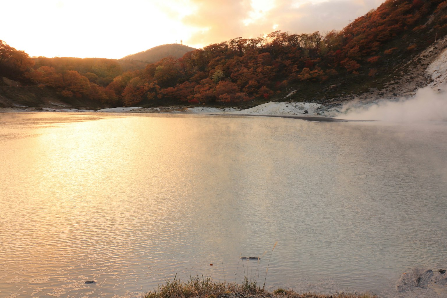Lago sereno che riflette il tramonto con foglie autunnali