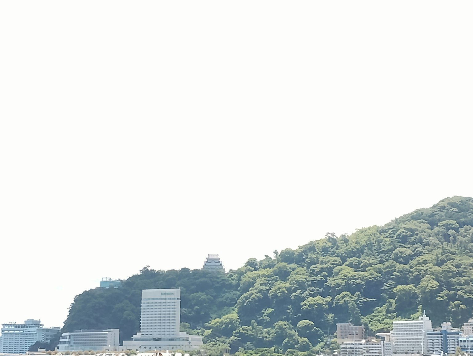 海岸景观，绿意盎然的山丘和现代建筑在晴朗的蓝天下