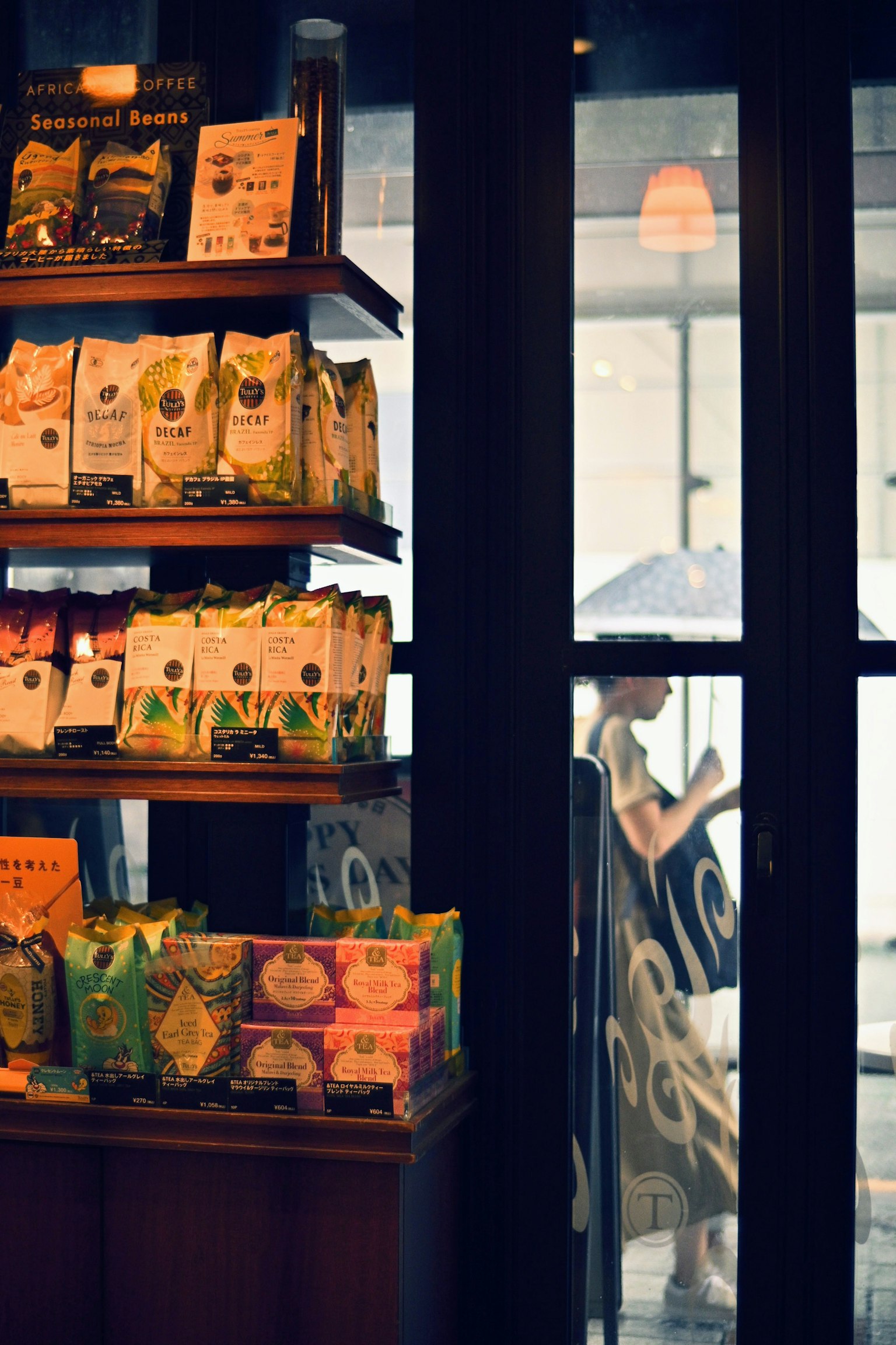 Colorful coffee bean packages on a shelf in a coffee shop with a person using a smartphone outside