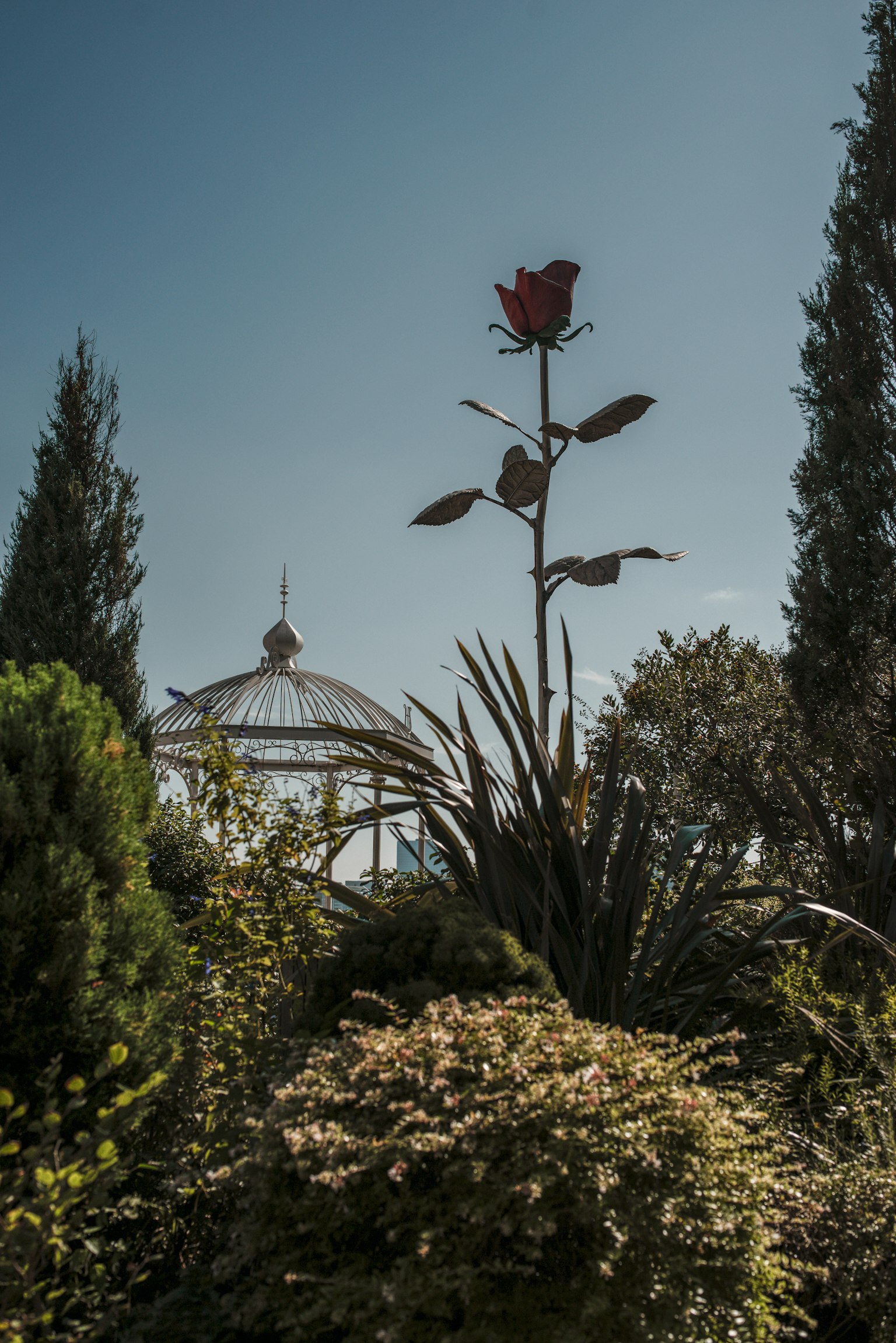 A tall red flower against a blue sky with lush greenery surrounding it