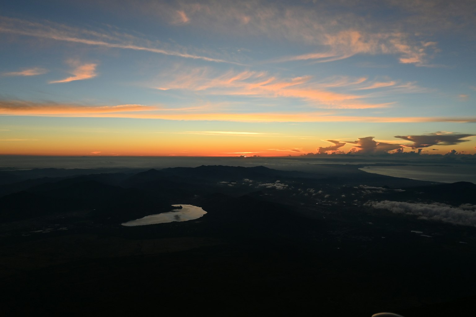 Wunderschöner Sonnenuntergangshimmel mit Silhouetten von Bergen und einem See